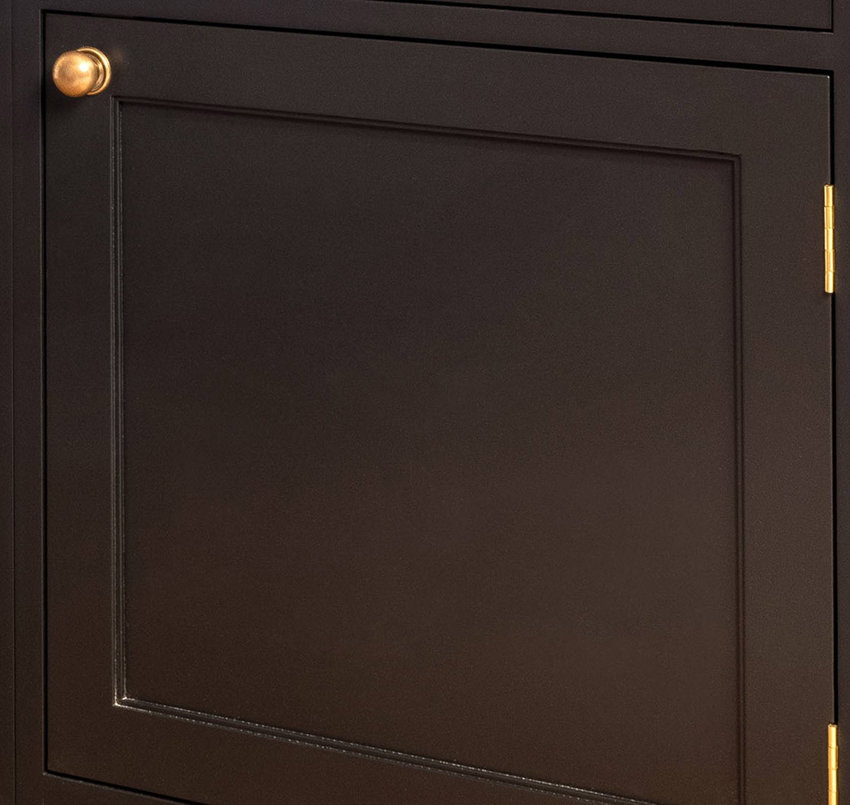A close-up of a dark brown cabinet door with a gold knob on the upper left corner and a gold hinge on the right edge. The door has a simple, recessed panel design.