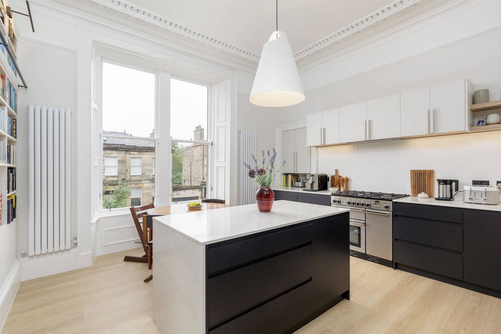 Stunning view of the Howard Place kitchen from an angle showcasing the intricate details and carefully curated design elements. The contrast between black and white cabinetry creates a captivating visual interplay, while the spacious island with sleek waterfall edge seamlessly integrates with the dining area.
