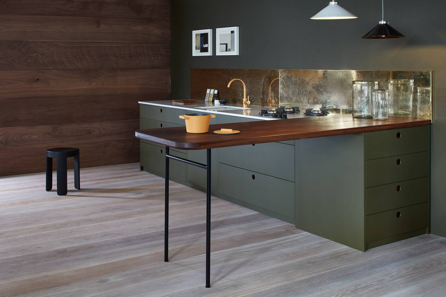 Dark green kitchen with brass coloured splashback and walnut work surface.