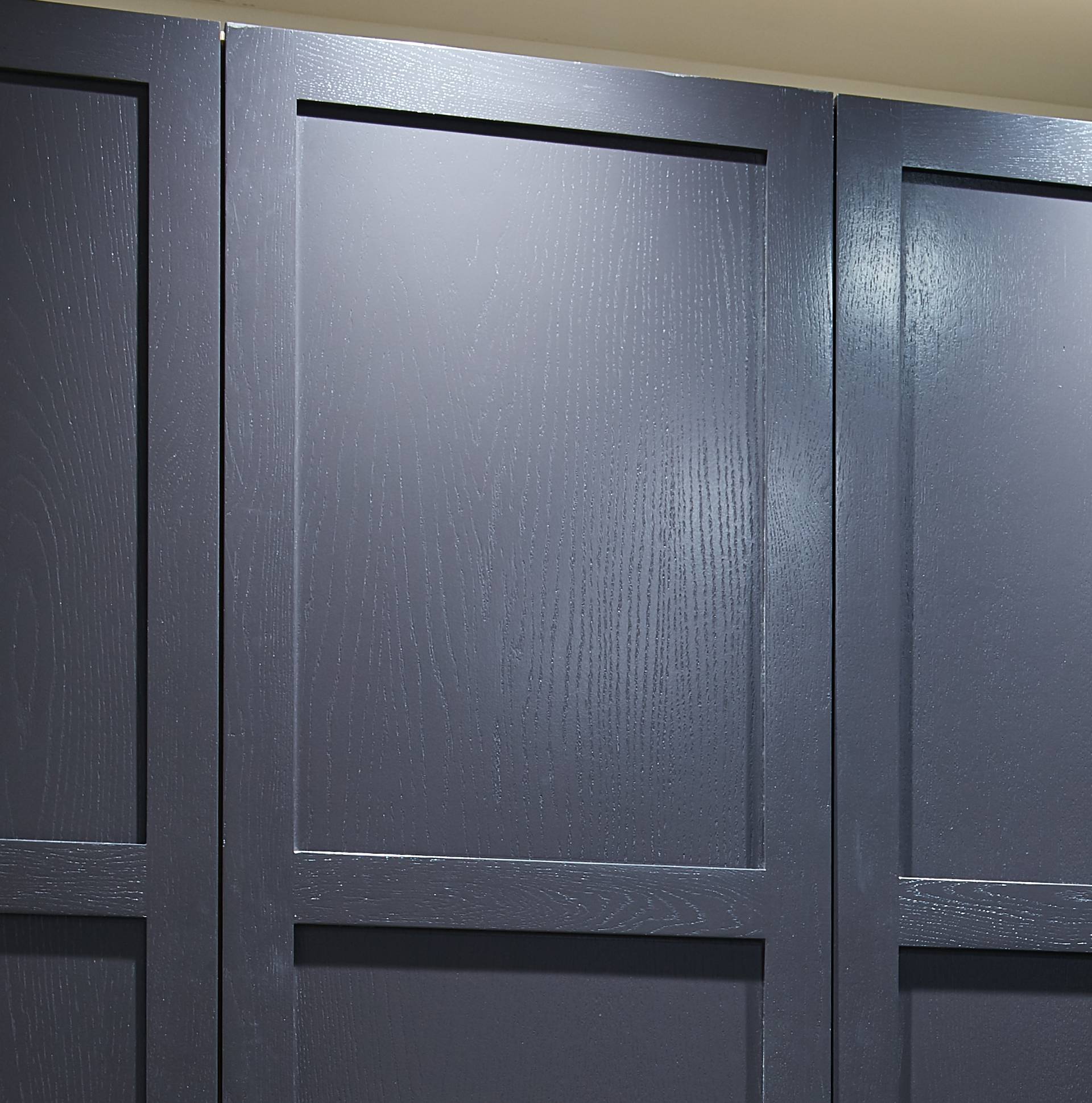 Close-up of three dark gray or black wooden panels with a smooth, matte finish and rectangular framing, possibly part of cabinetry or wall paneling.