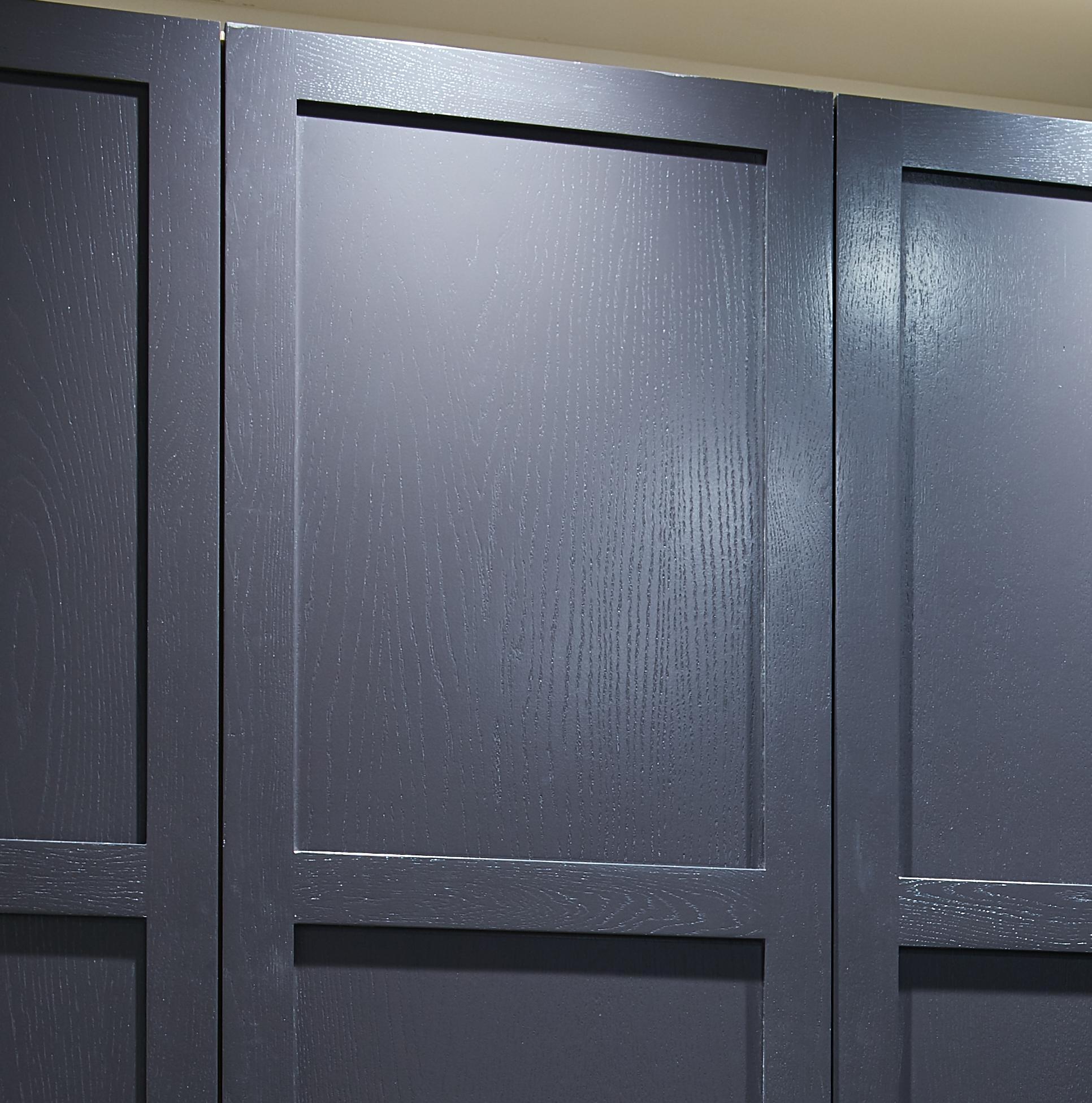 Close-up of three dark gray or black wooden panels with a smooth, matte finish and rectangular framing, possibly part of cabinetry or wall paneling.
