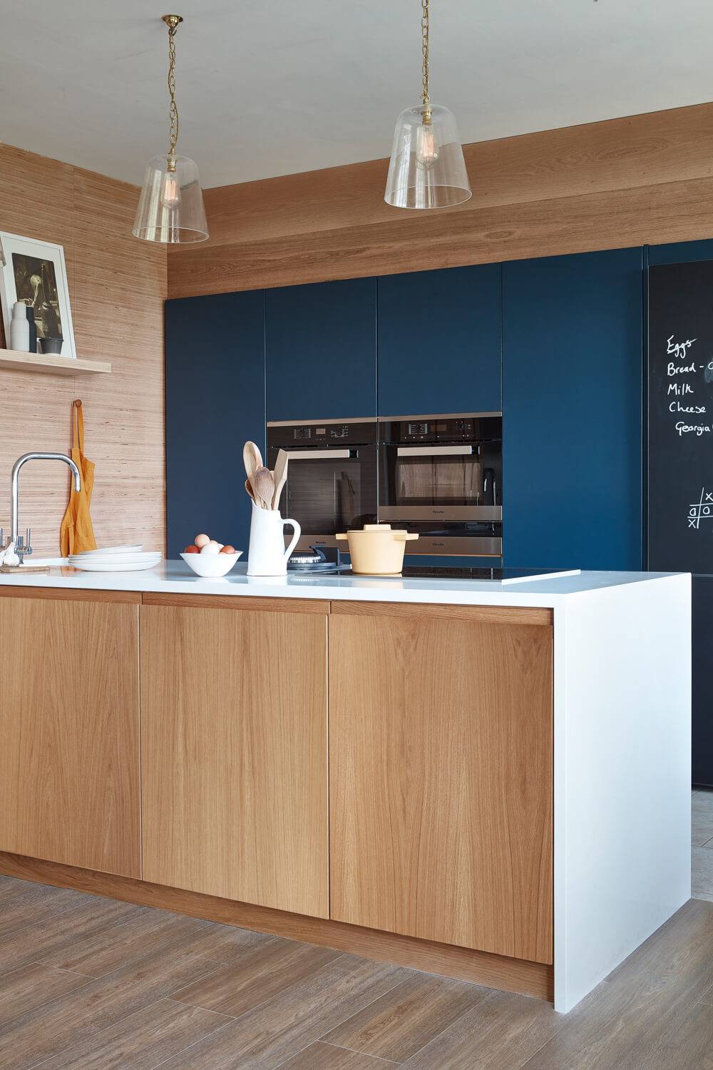 Sleek J-groove handles add subtle character to blue painted doors, harmonizing with natural waterfall style worktop in this compact kitchen. 