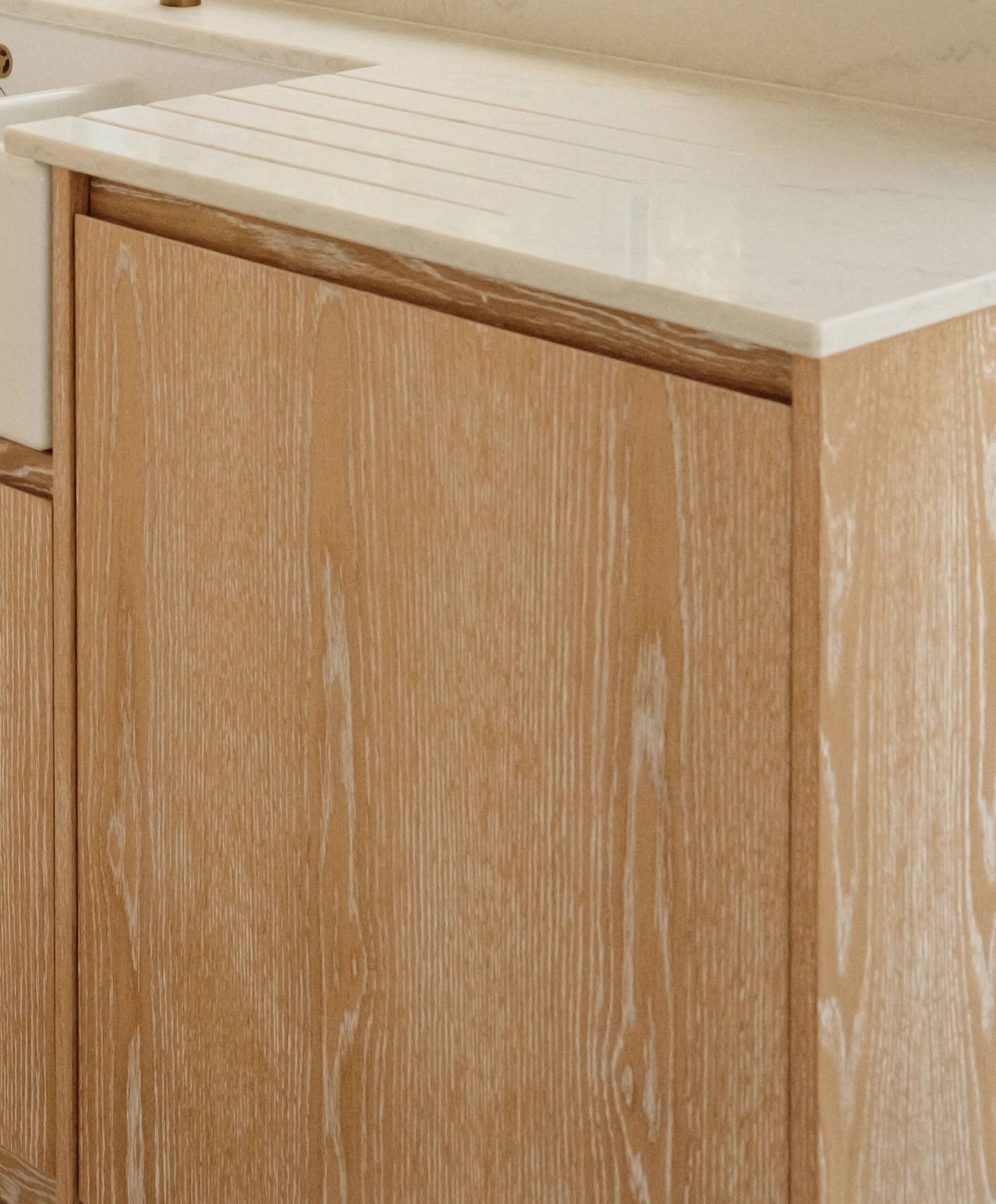 Light wood kitchen cabinet with a white stone countertop and an integrated sink, featuring a minimalist and clean design.