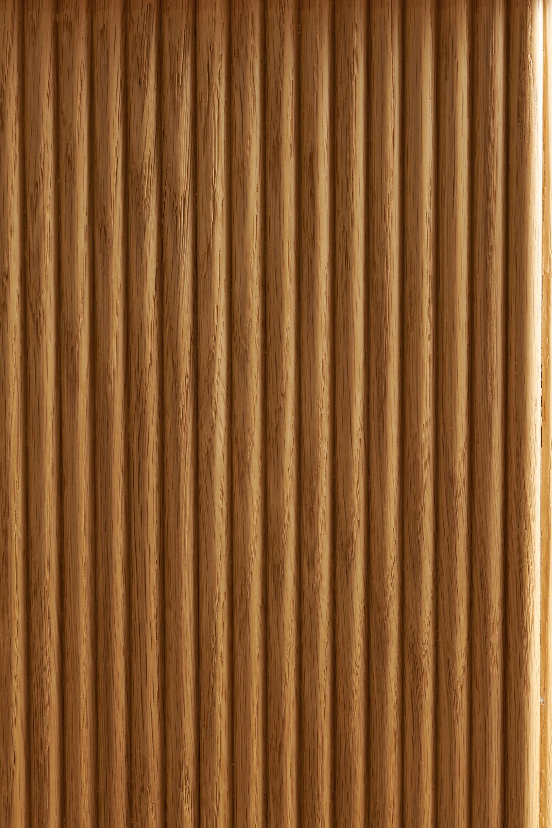 Wooden surface with vertical grooves resembling a corrugated texture, displaying a light brown color and natural wood grain patterns.