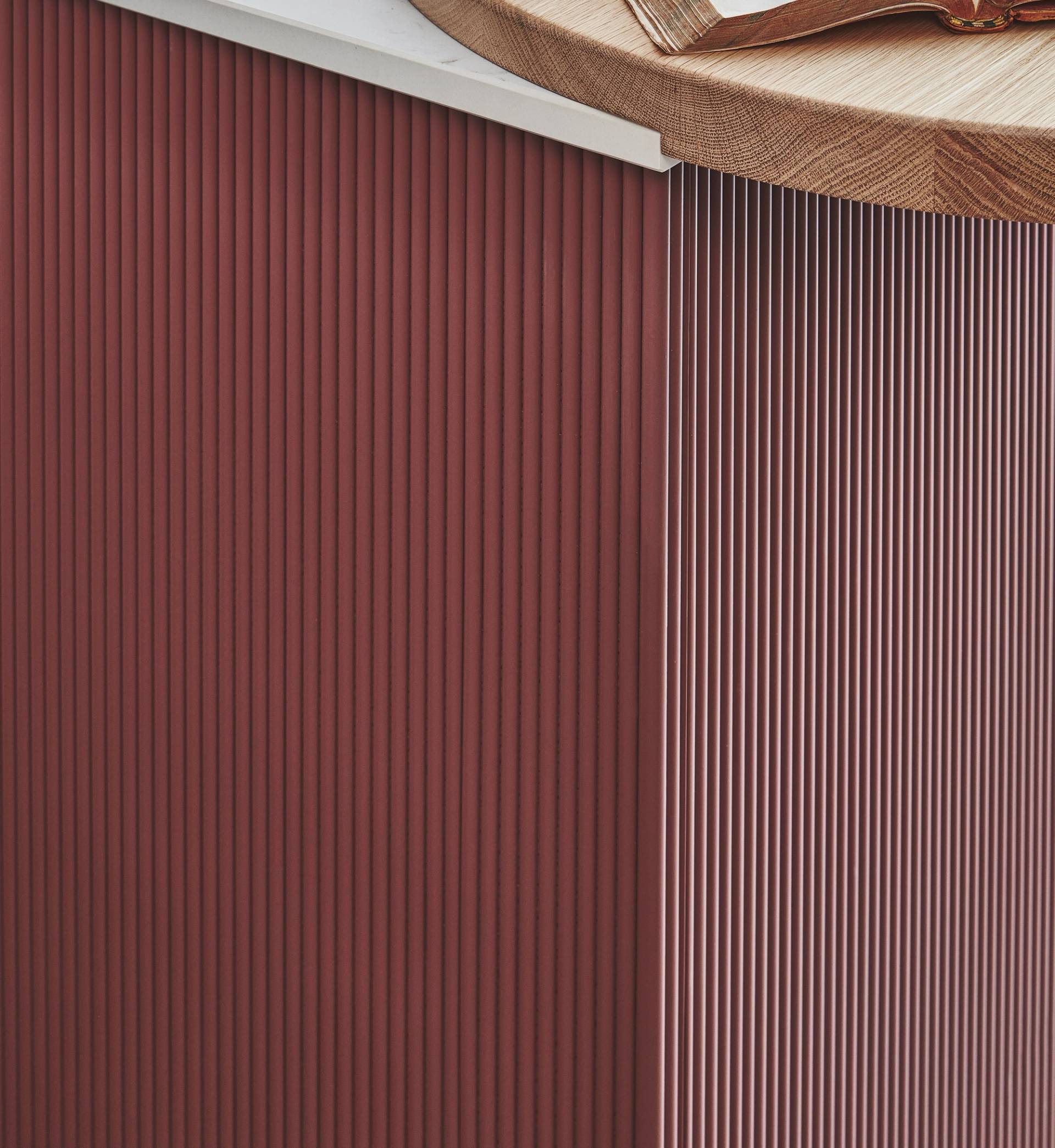 Close-up of a corner of a piece of furniture with vertical red ridges and a wooden top, showing detailed texture and clean, modern lines.