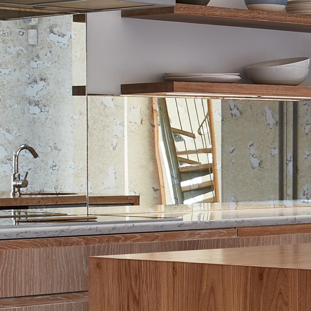 A modern kitchen with wooden shelves holding dishes, a marble countertop, and a mirrored backsplash reflecting a faucet and a rustic textured wall.