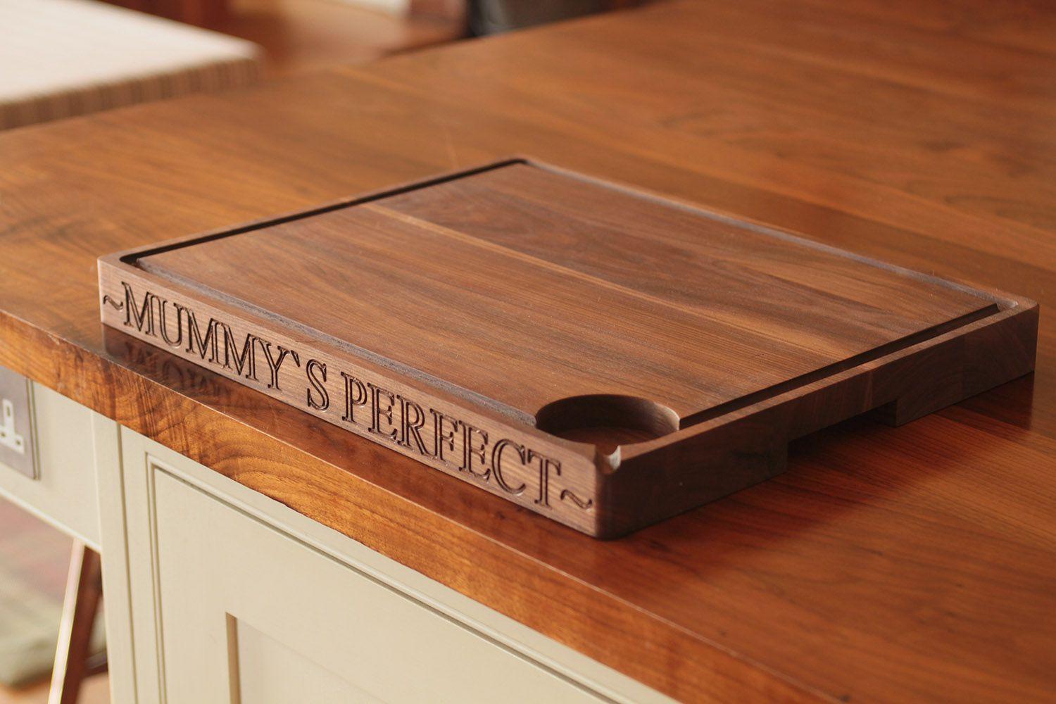 Wooden chopping board on a kitchen counter, featuring carved text that reads 'mummys perfect'