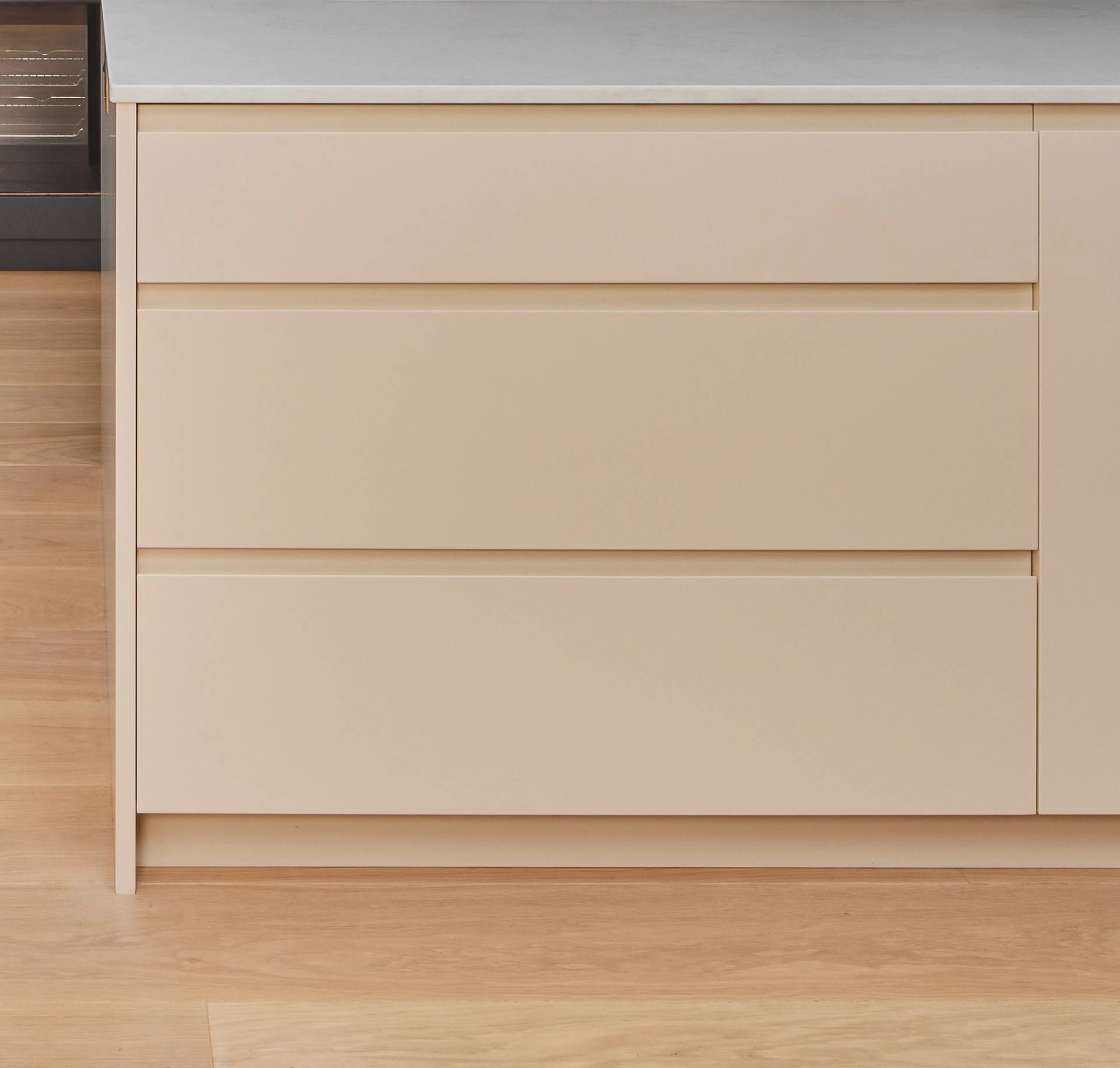 A close-up view of a modern kitchen island with three beige drawers and a white countertop, set on a light wooden floor.