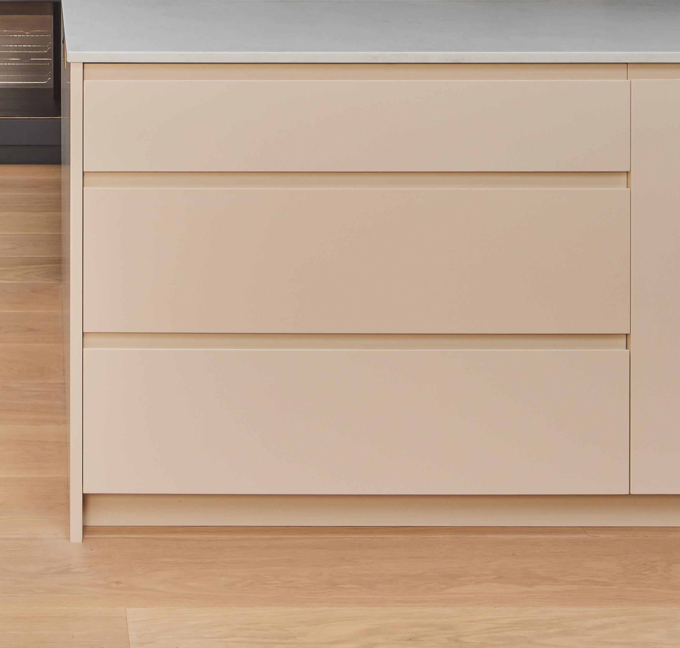 A close-up view of a modern kitchen island with three beige drawers and a white countertop, set on a light wooden floor.