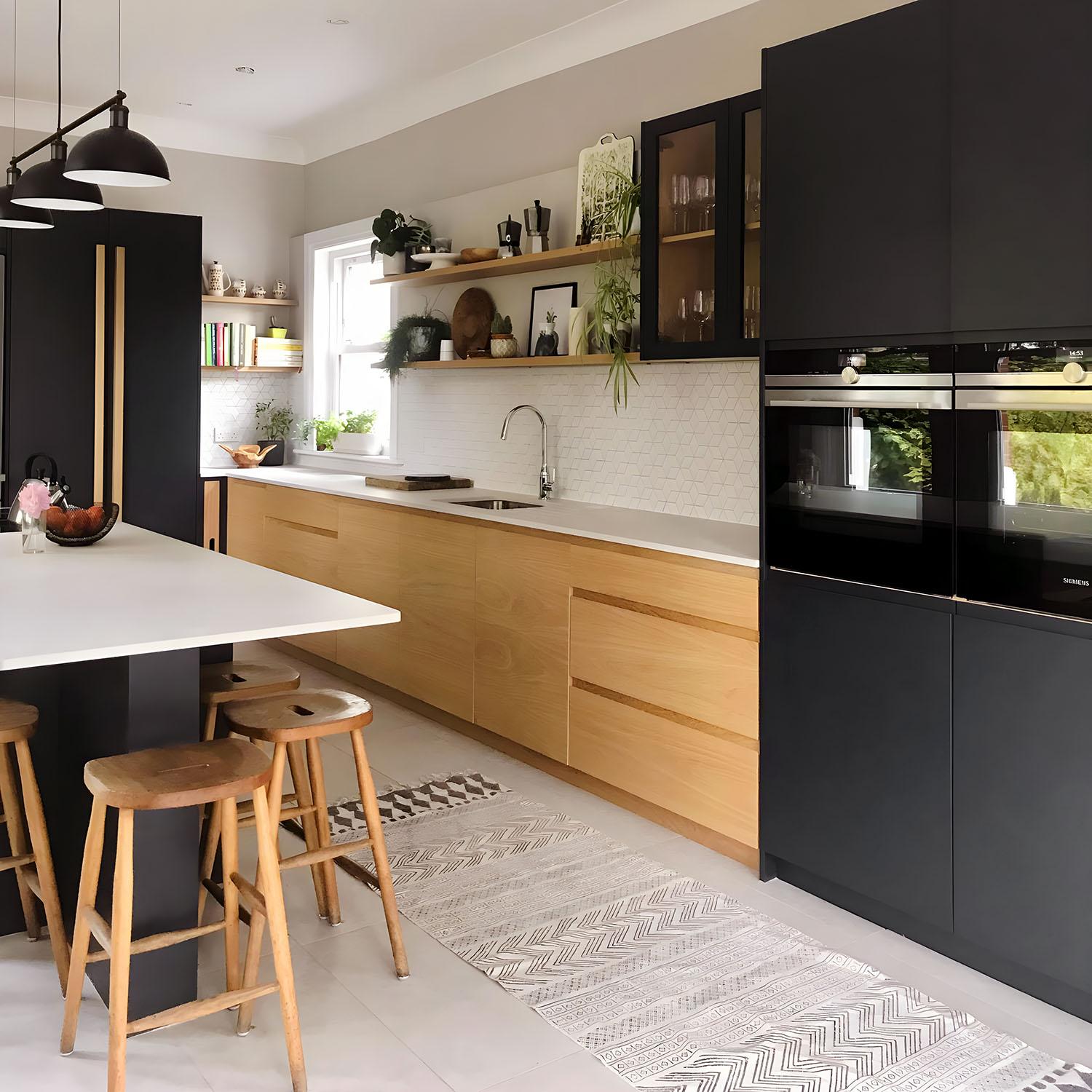 Modern kitchen with black and light wood cabinets, a white island with wooden stools, built-in black appliances, open shelving with plants and dishes, a patterned rug, and a large window providing natural light.