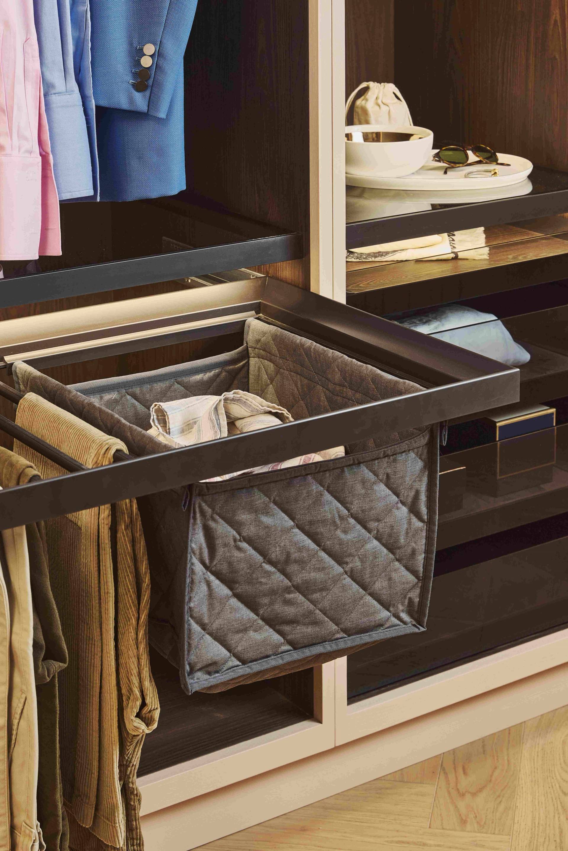 A sleek, modern wardrobe with dark wood doors, some of which are open revealing wooden drawers inside. Clothes, including a jacket, are neatly hung. The carpeted floor adds warmth to the space.