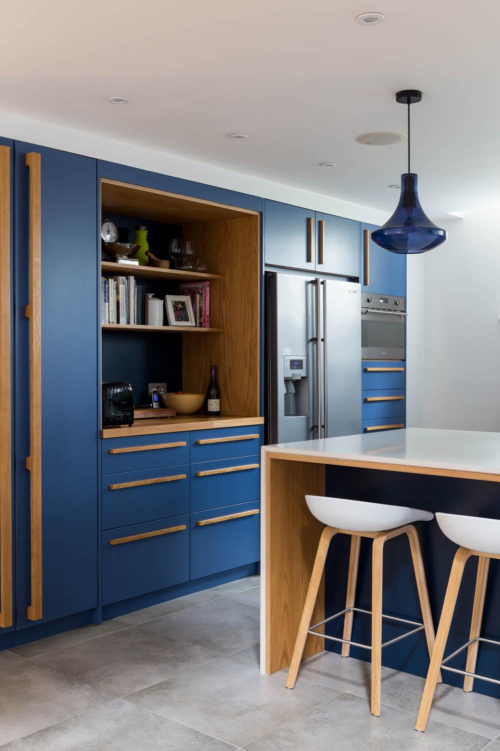Striking custom blue cabinets define the space, accented by warm oak bar handles and chrome appliances, creating a timeless yet effortless feel.
