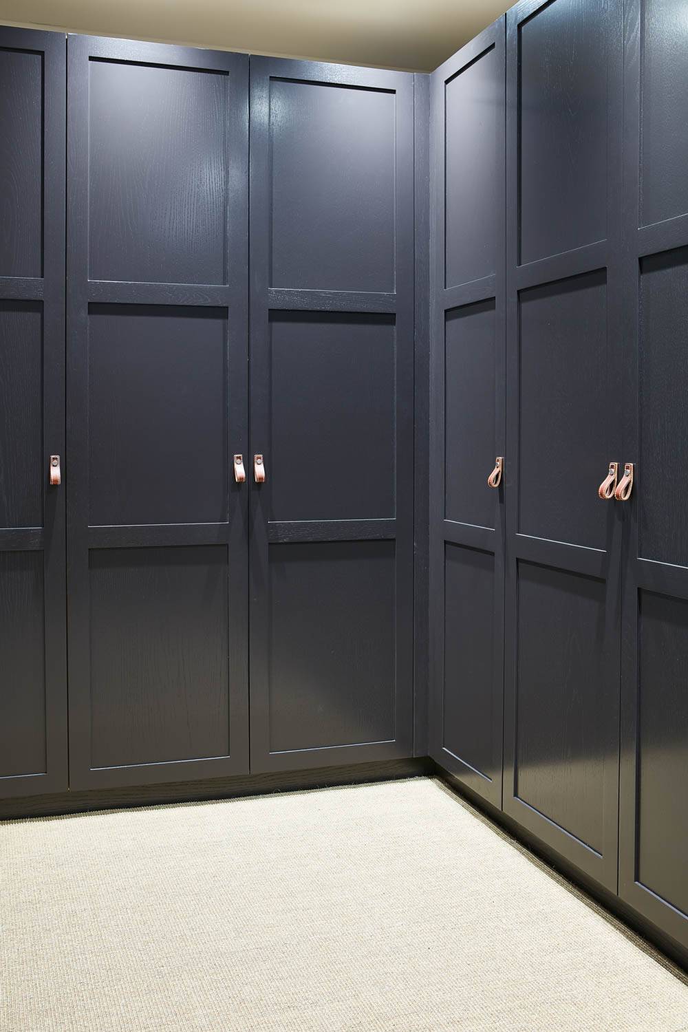 A modern dark wood wardrobe with one door open, revealing wooden drawers, neatly folded clothes, and a hanging jacket inside. The wardrobe stands on a light-colored carpeted floor