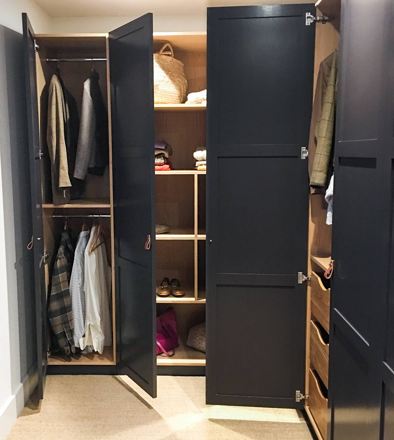 A modern wardrobe with open black doors reveals hanging clothes, shelves with baskets, shoes, folded garments, and drawers, all organized neatly inside a wooden interior.
