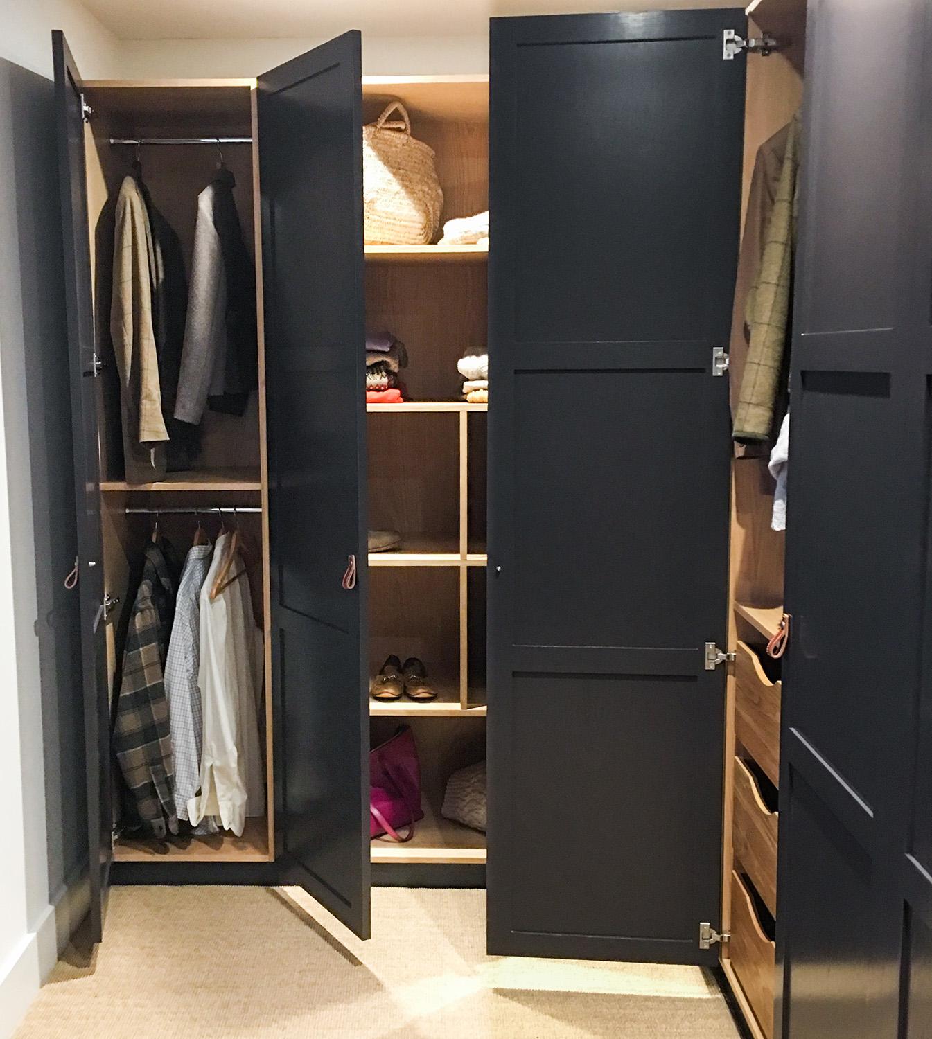 A modern wardrobe with open black doors reveals hanging clothes, shelves with baskets, shoes, folded garments, and drawers, all organized neatly inside a wooden interior.