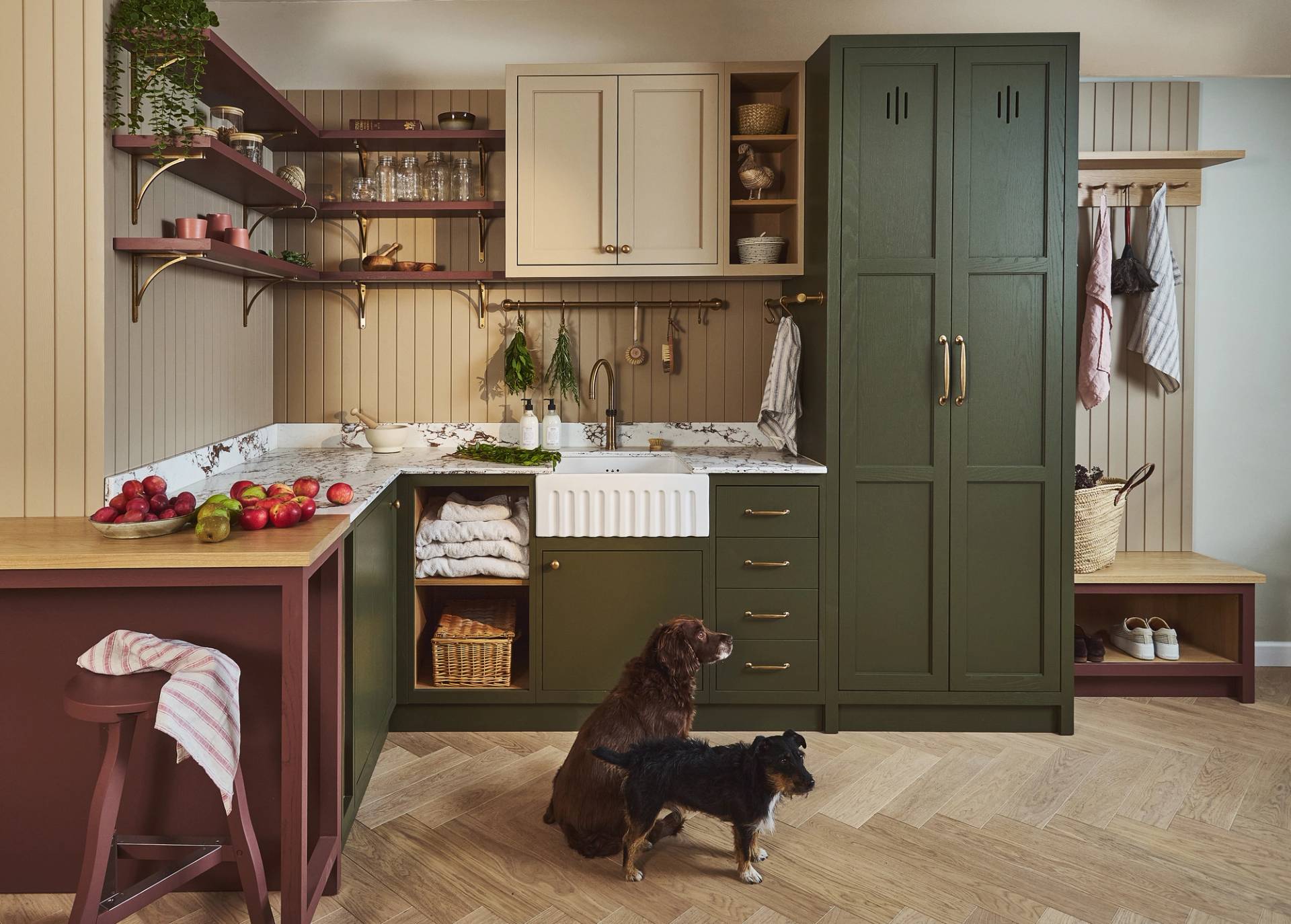 Utility room with green and cream cabinets, open shelves, farmhouse sink, wooden accents, and a countertop with fruit and folded linens.