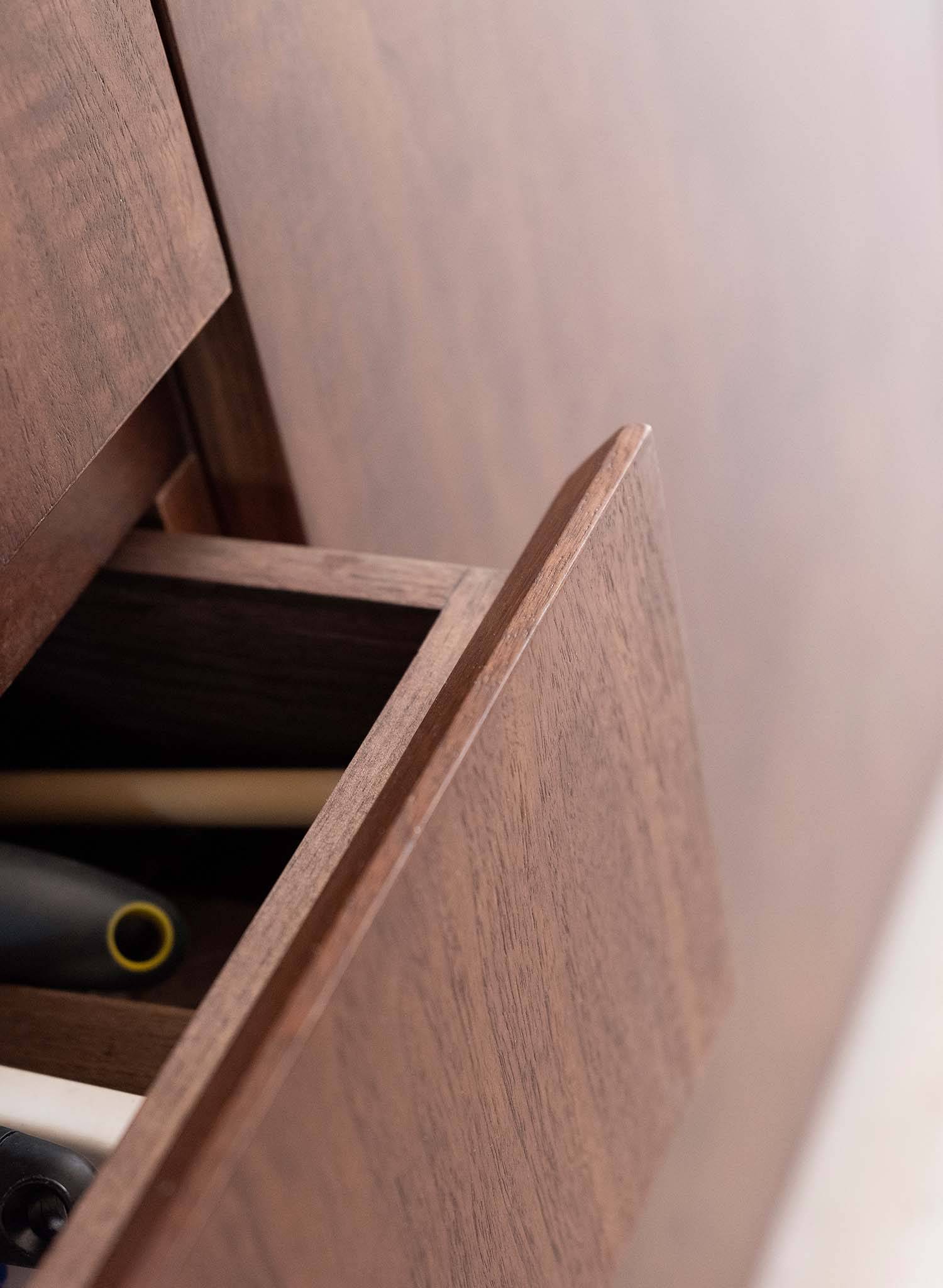 Close-up of an open wooden drawer in a cabinet, revealing neatly stored pens and pencils. The wood has a smooth finish, adding a polished look to the furniture piece