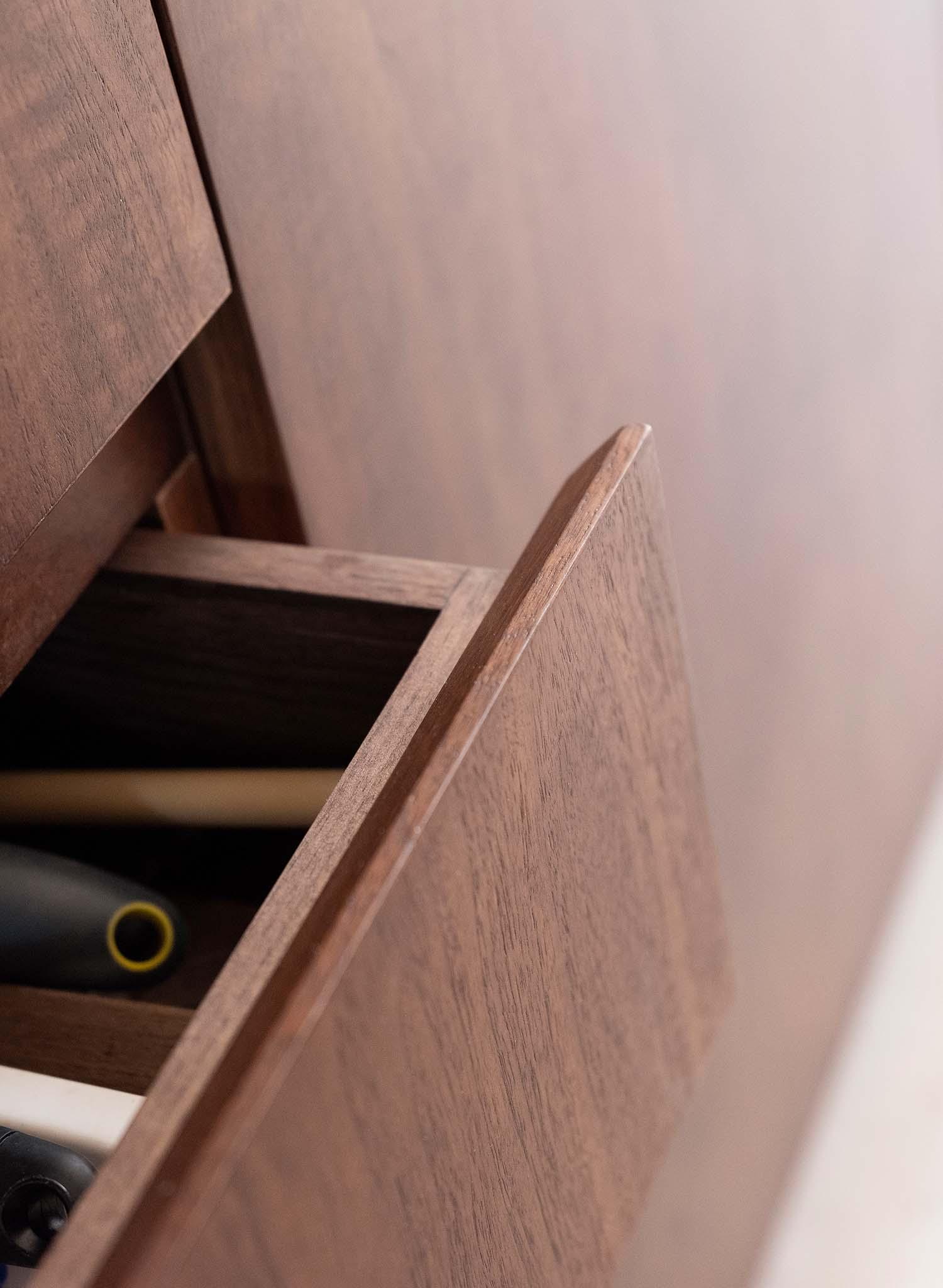 Close-up of an open wooden drawer in a cabinet, revealing neatly stored pens and pencils. The wood has a smooth finish, adding a polished look to the furniture piece