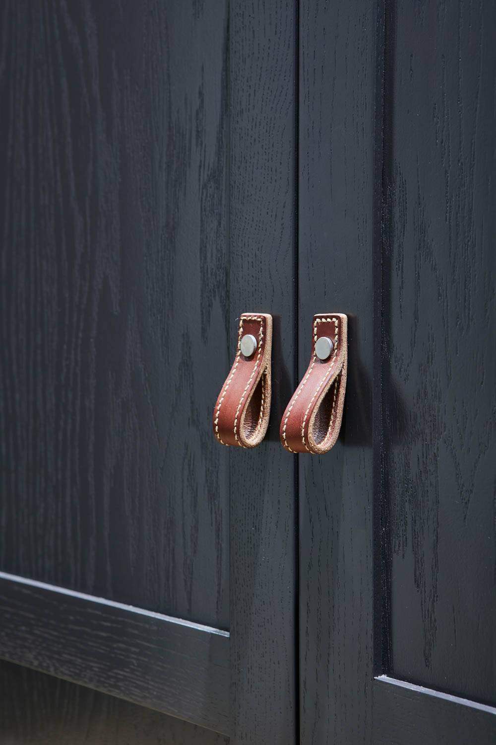 Close-up of dark wooden cabinet doors with brown leather loop handles, each secured by a metal rivet
