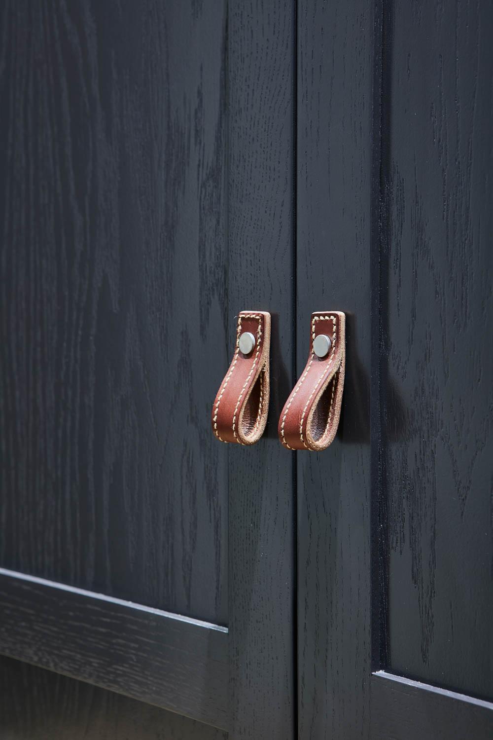 Close-up of dark wooden cabinet doors with brown leather loop handles, each secured by a metal rivet