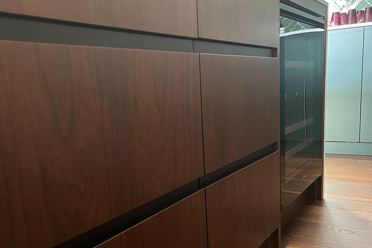 Wooden cabinets with dark, sleek paneling are arranged in a modern kitchen setting, reflecting light subtly