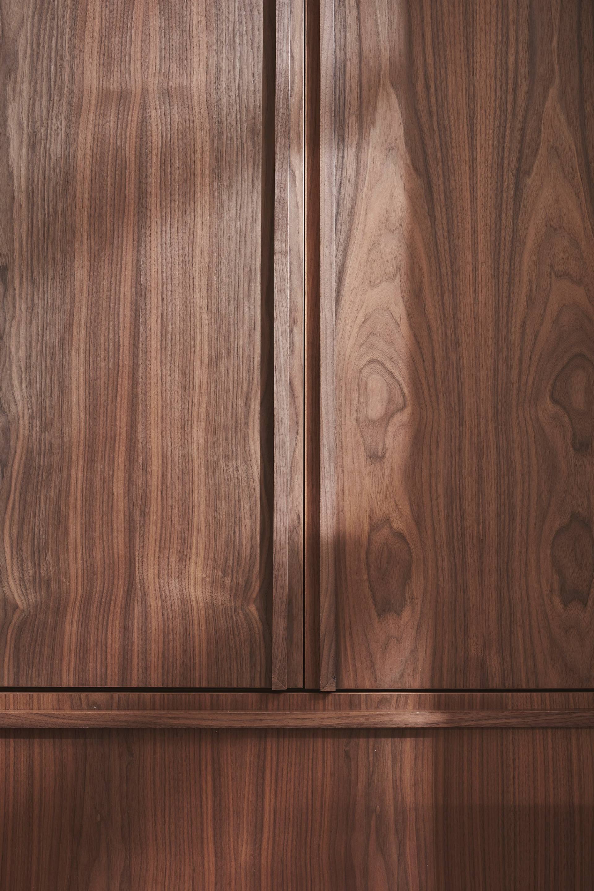 Wooden cabinet doors with a vertical seam in the center, featuring a natural wood grain pattern. Light and shadow play across the surface, highlighting the texture and variety in the wood.