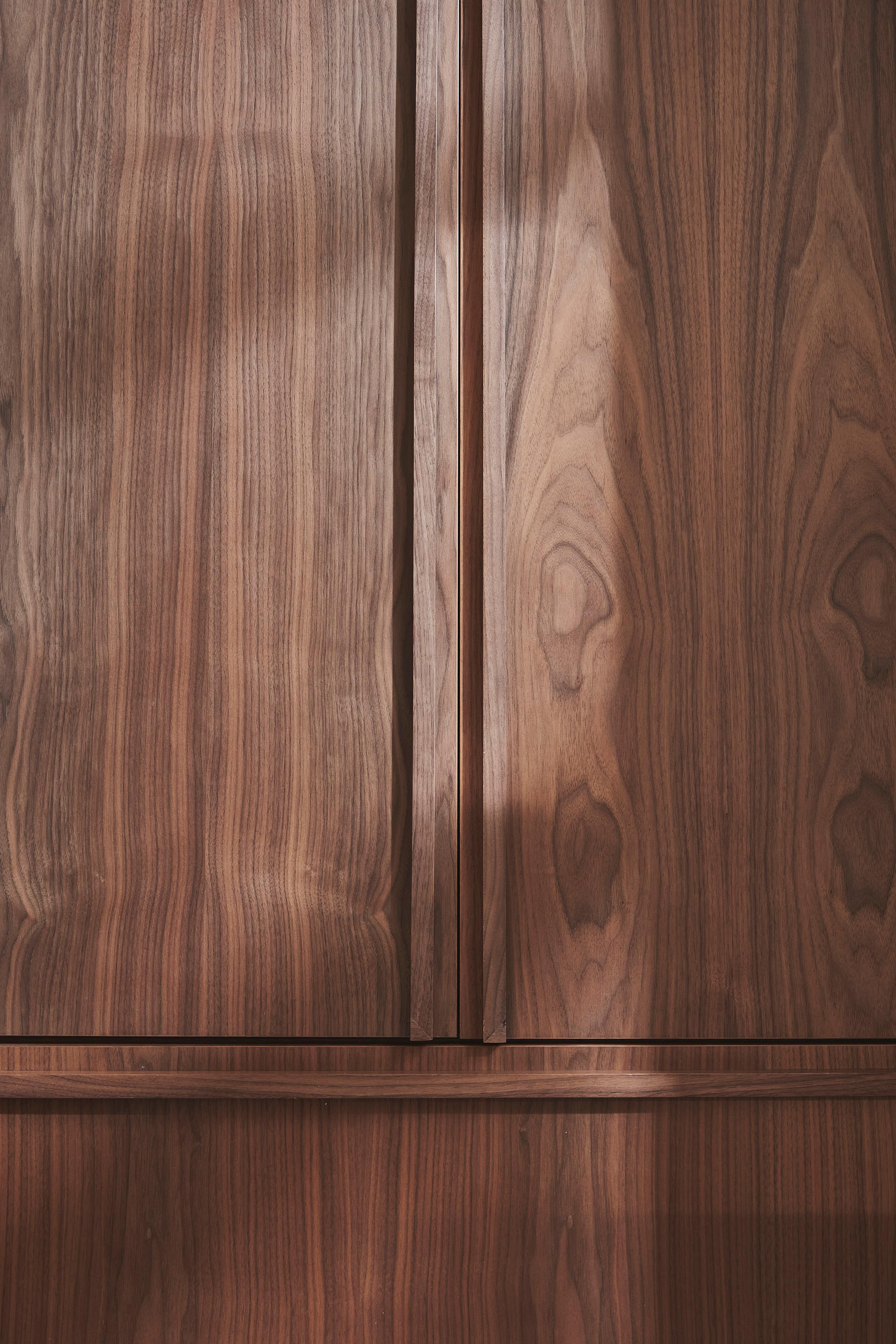 Wooden cabinet doors with a vertical seam in the center, featuring a natural wood grain pattern. Light and shadow play across the surface, highlighting the texture and variety in the wood.