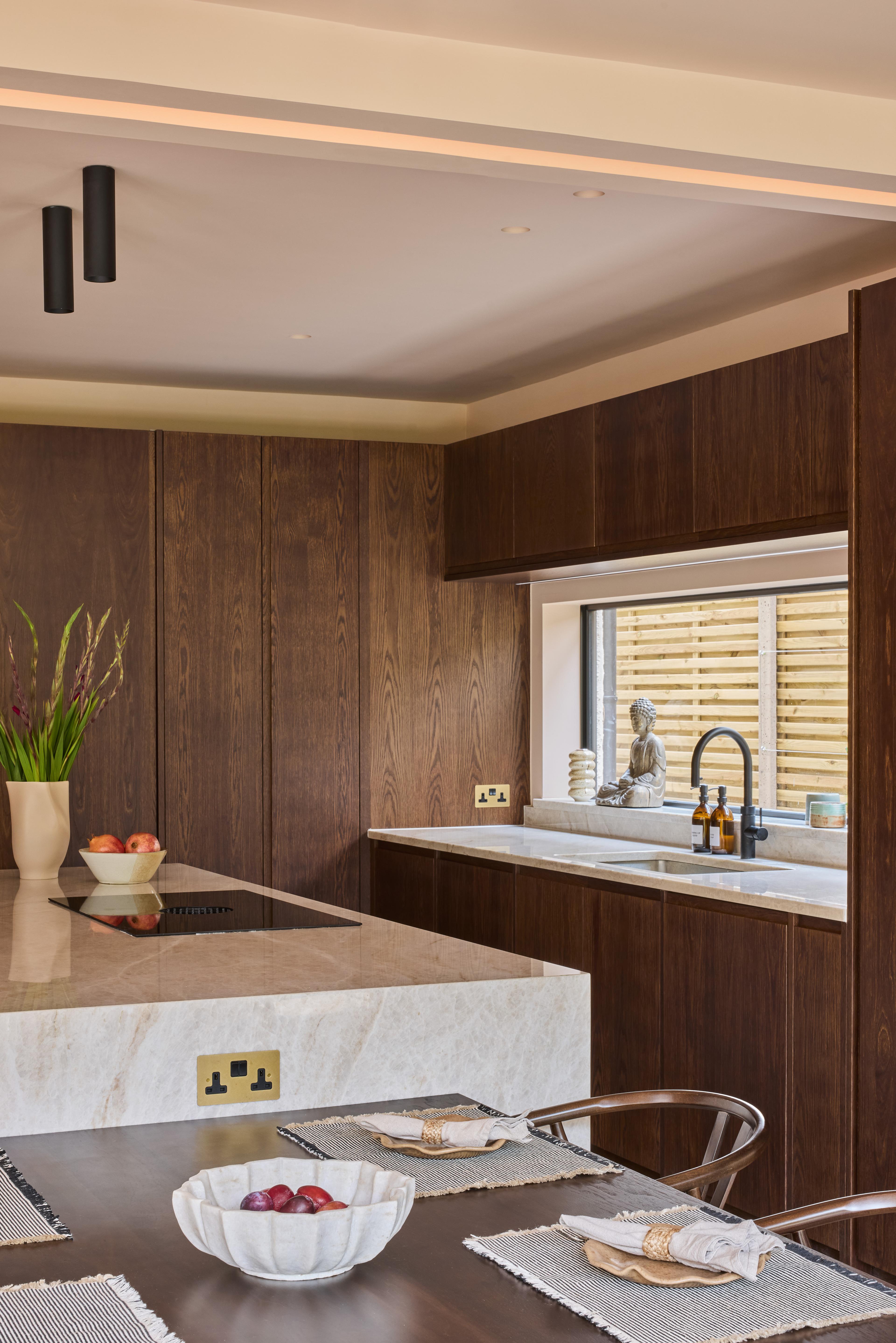 A wooden cabinet with glass doors displaying ceramic dishes, bowls, and a jug. Below is a light blue drawer set with a marbled countertop. Warm lighting highlights the textures and tones of the ceramics and wood