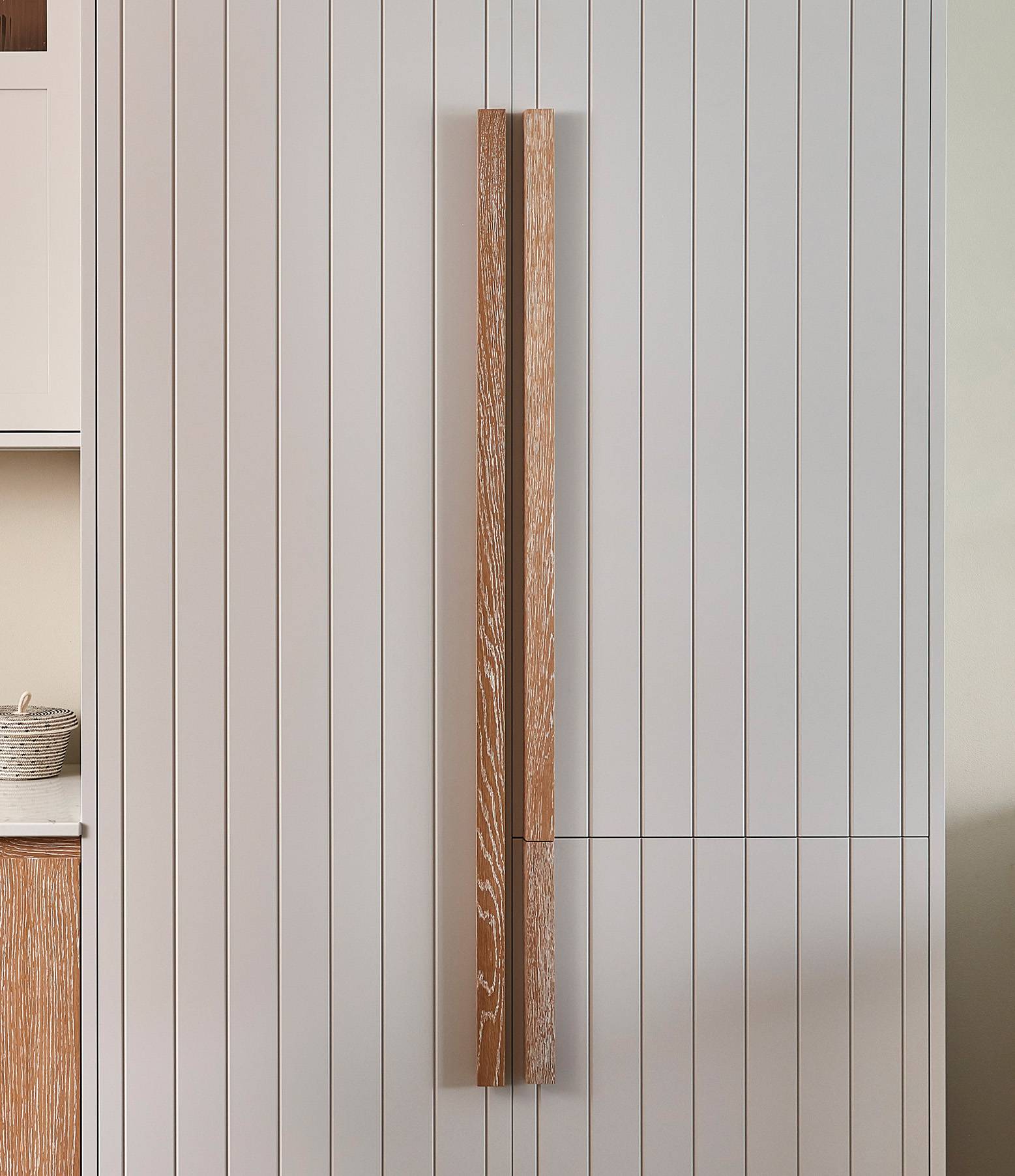 A sleek wooden door with vertical grooves and two thin wooden handles is set against a paneled wall. The doors light wood contrasts subtly with the walls neutral tone, lending a minimalist and modern appearance.