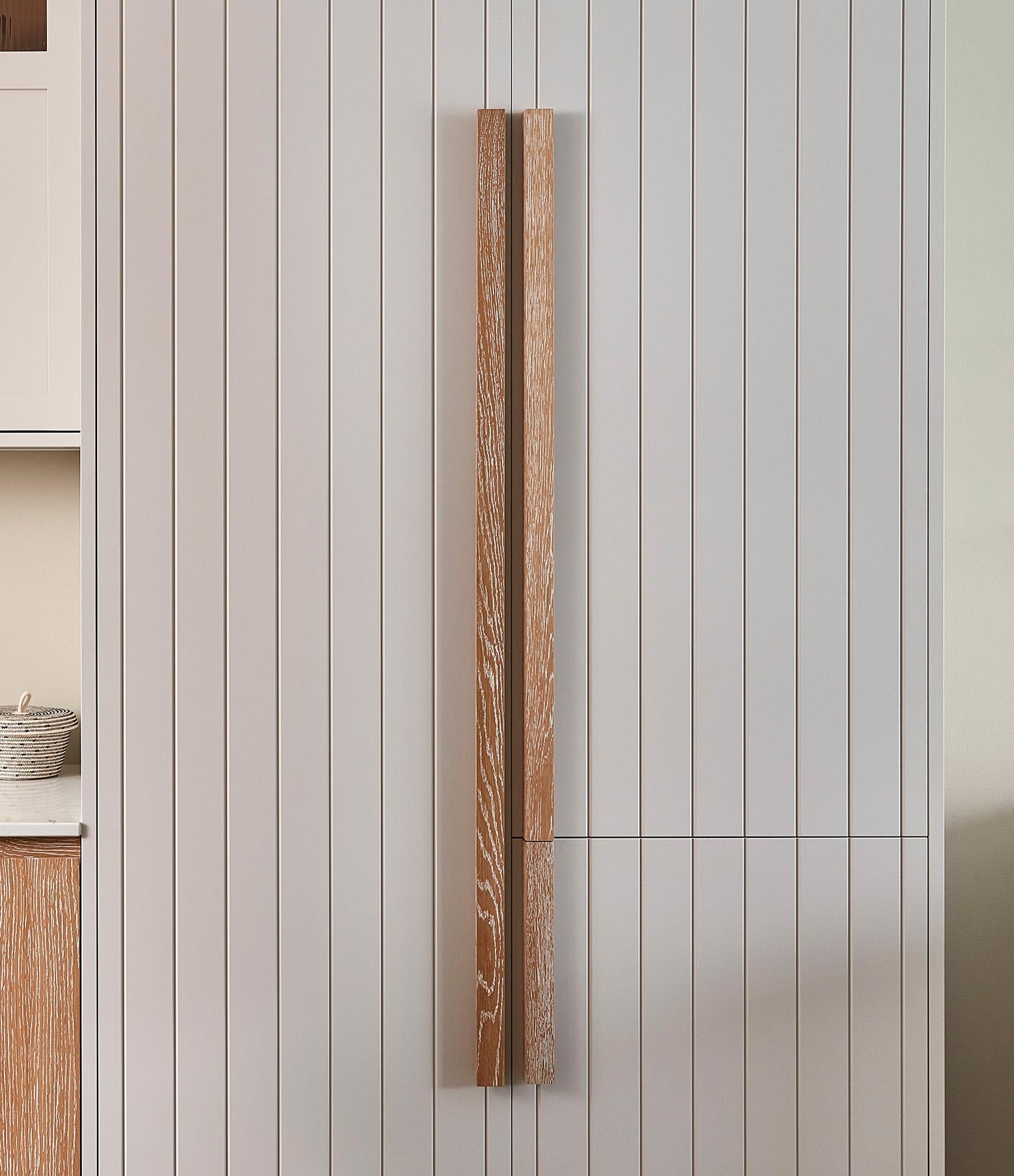 A sleek wooden door with vertical grooves and two thin wooden handles is set against a paneled wall. The doors light wood contrasts subtly with the walls neutral tone, lending a minimalist and modern appearance.