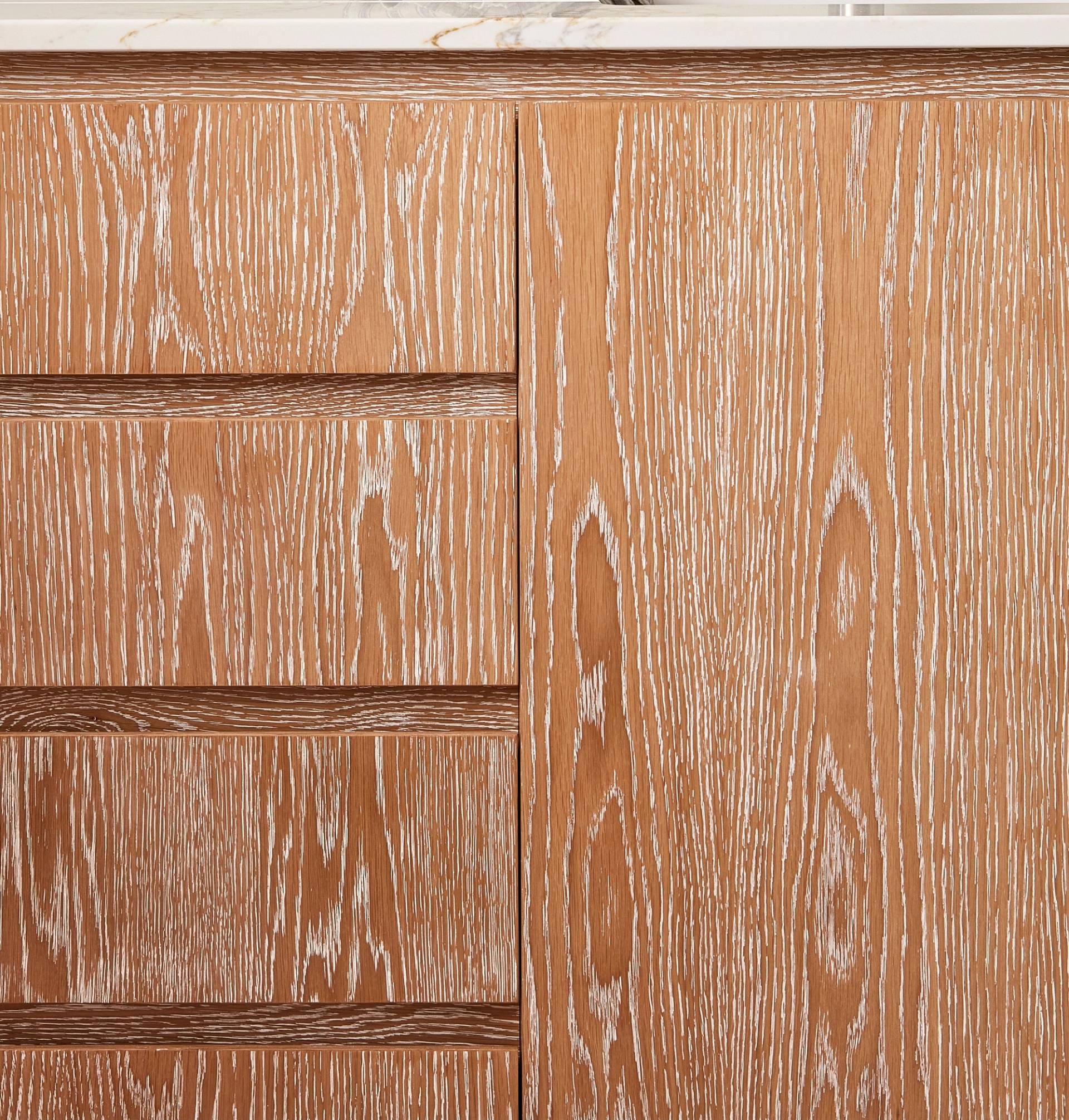 Close-up of a wooden cabinet with a light brown finish, displaying a prominent grain pattern. The design includes vertical and horizontal grooves, with a smooth, glossy surface.