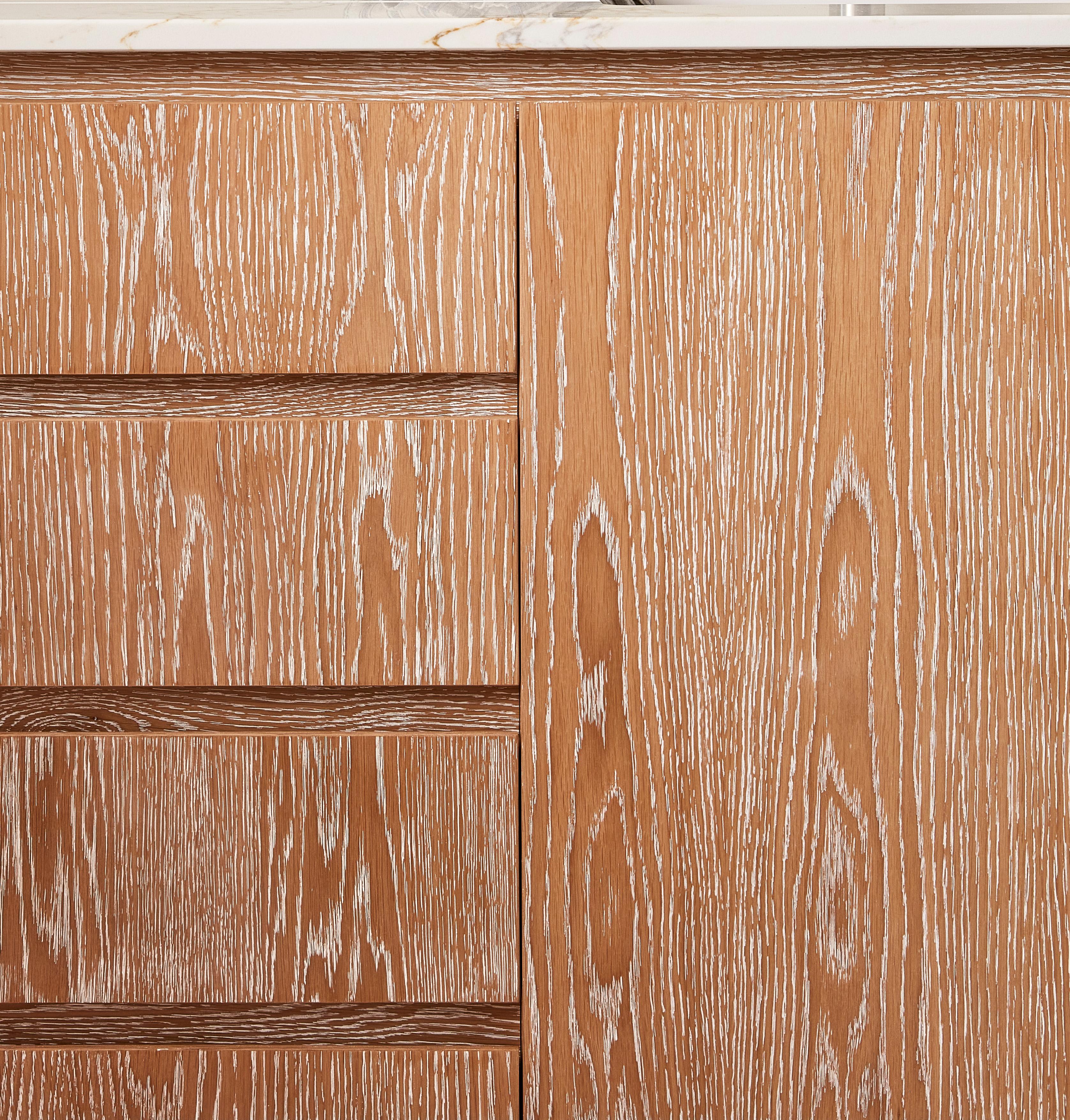 Close-up of a wooden cabinet with a light brown finish, displaying a prominent grain pattern. The design includes vertical and horizontal grooves, with a smooth, glossy surface.