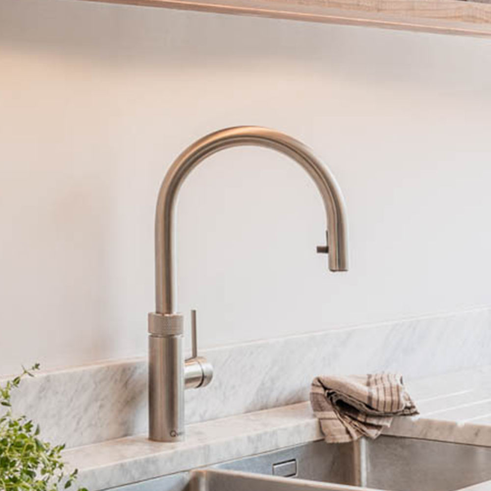 A modern kitchen sink with a stainless steel faucet. A striped dish towel is draped over the edge of the white marble countertop. A small green plant is partially visible on the left side.
