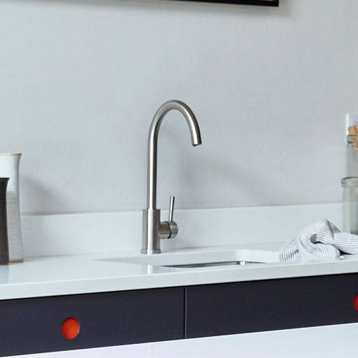 A modern kitchen countertop with a sleek, stainless steel faucet, a striped dish towel, a glass jar, a utensil holder, and white cabinetry with dark drawers featuring round orange handles.