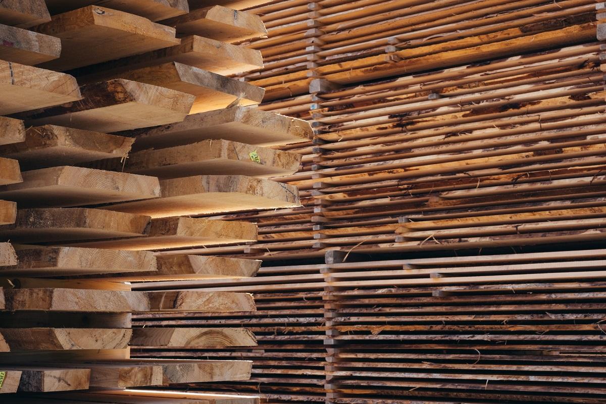 Large, neatly organized stacks of cut raw timber boards drying inside a lumber storage facility.