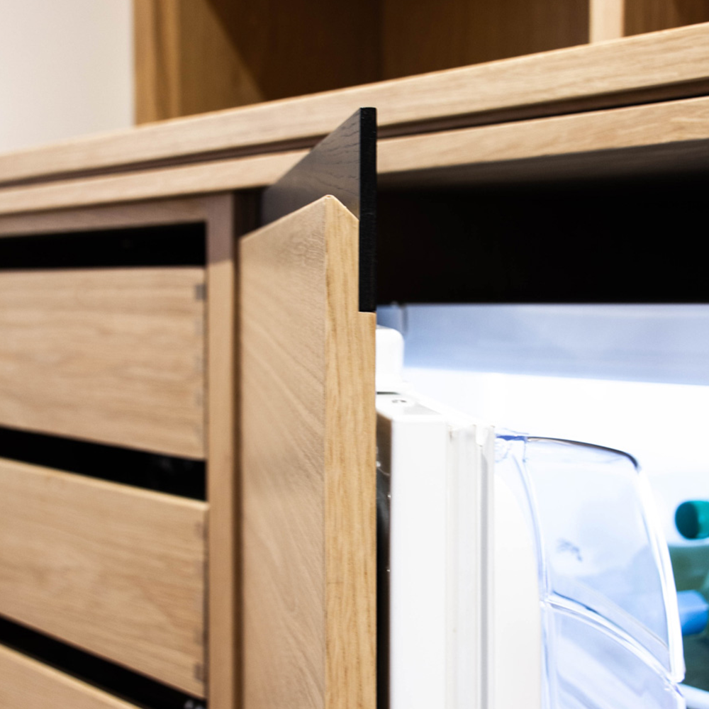 A built-in refrigerator with a wooden panel door is partially open, revealing the bright interior and clear shelves, blending seamlessly with the surrounding wooden cabinetry.