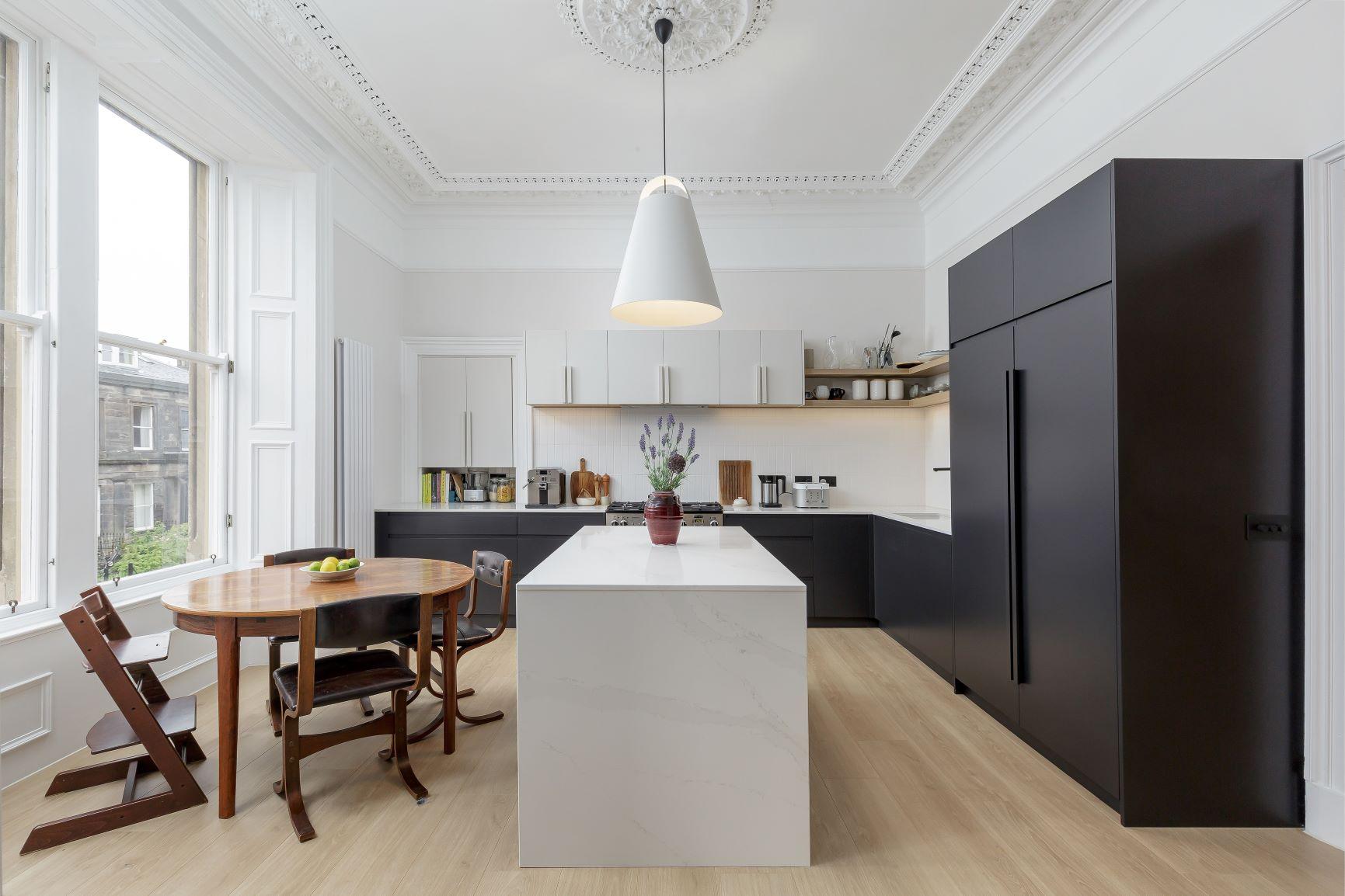 Modern kitchen with pastel blue cabinets and gold handles. Marble backsplash and countertop around a stainless steel oven and sink. Light wood herringbone floor. A yellow accent chair is partially visible in the foreground.