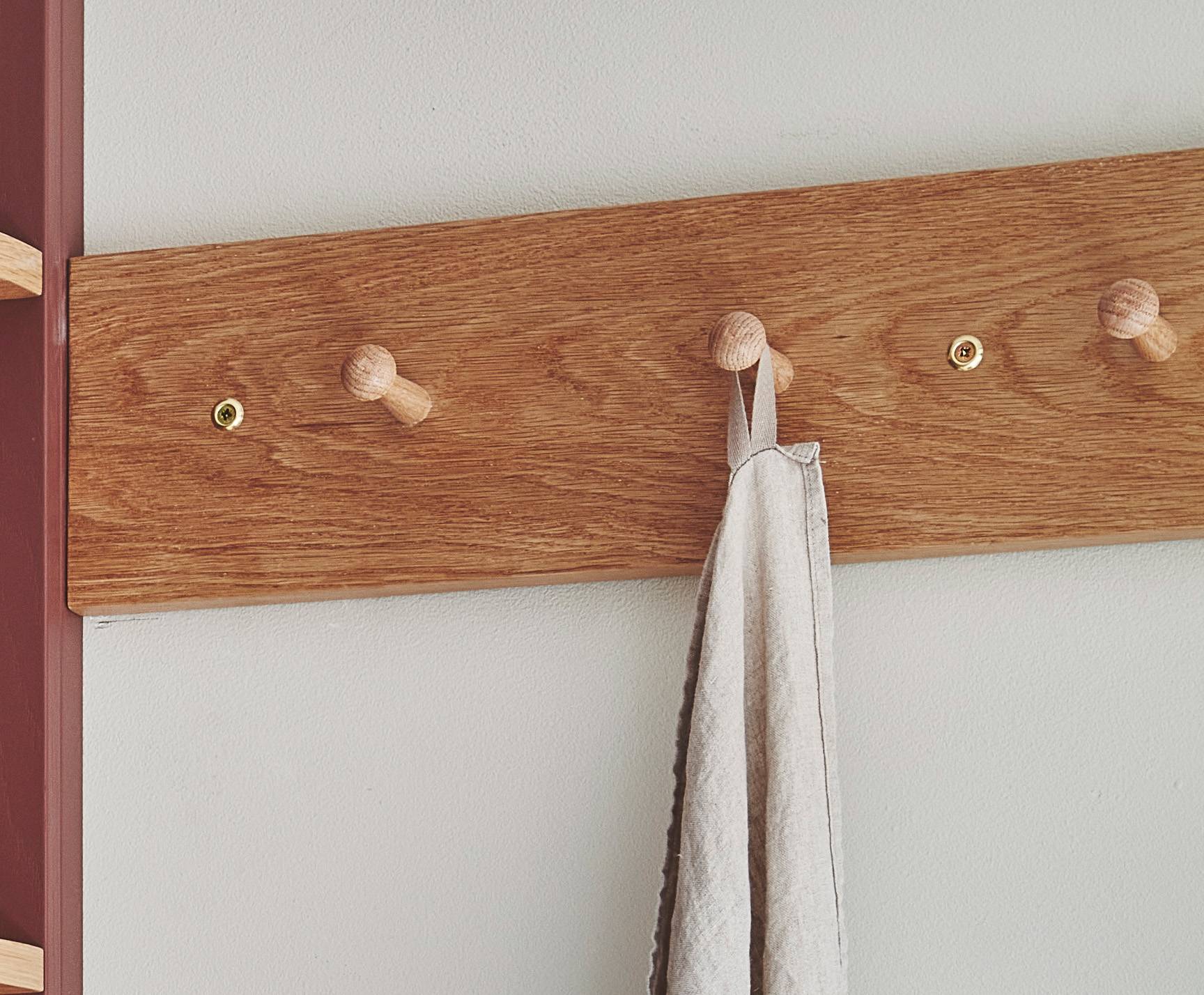 A wooden coat rack with four pegs is mounted on a white wall. A single gray towel hangs from the second peg from the left.