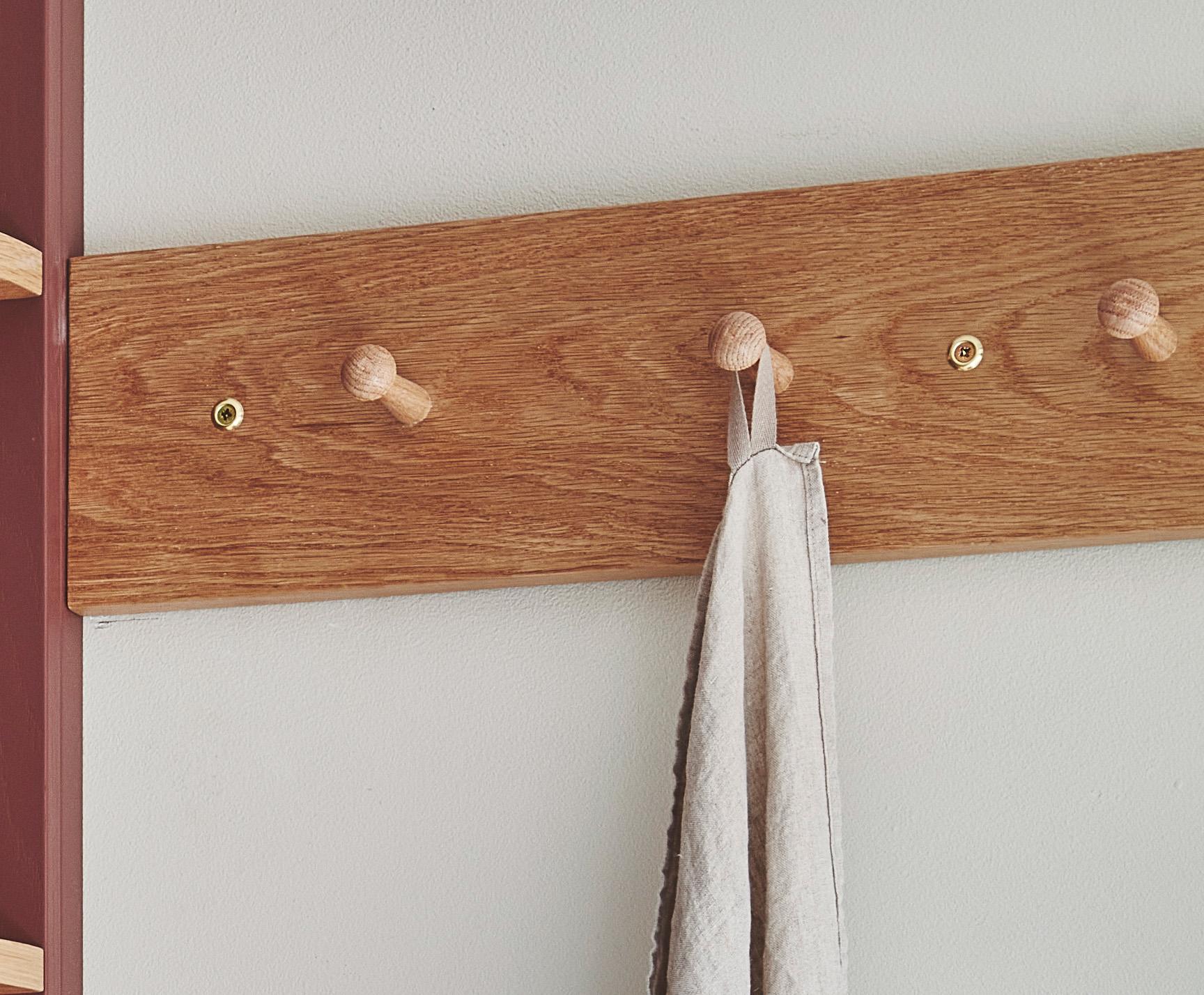 A wooden coat rack with four pegs is mounted on a white wall. A single gray towel hangs from the second peg from the left.