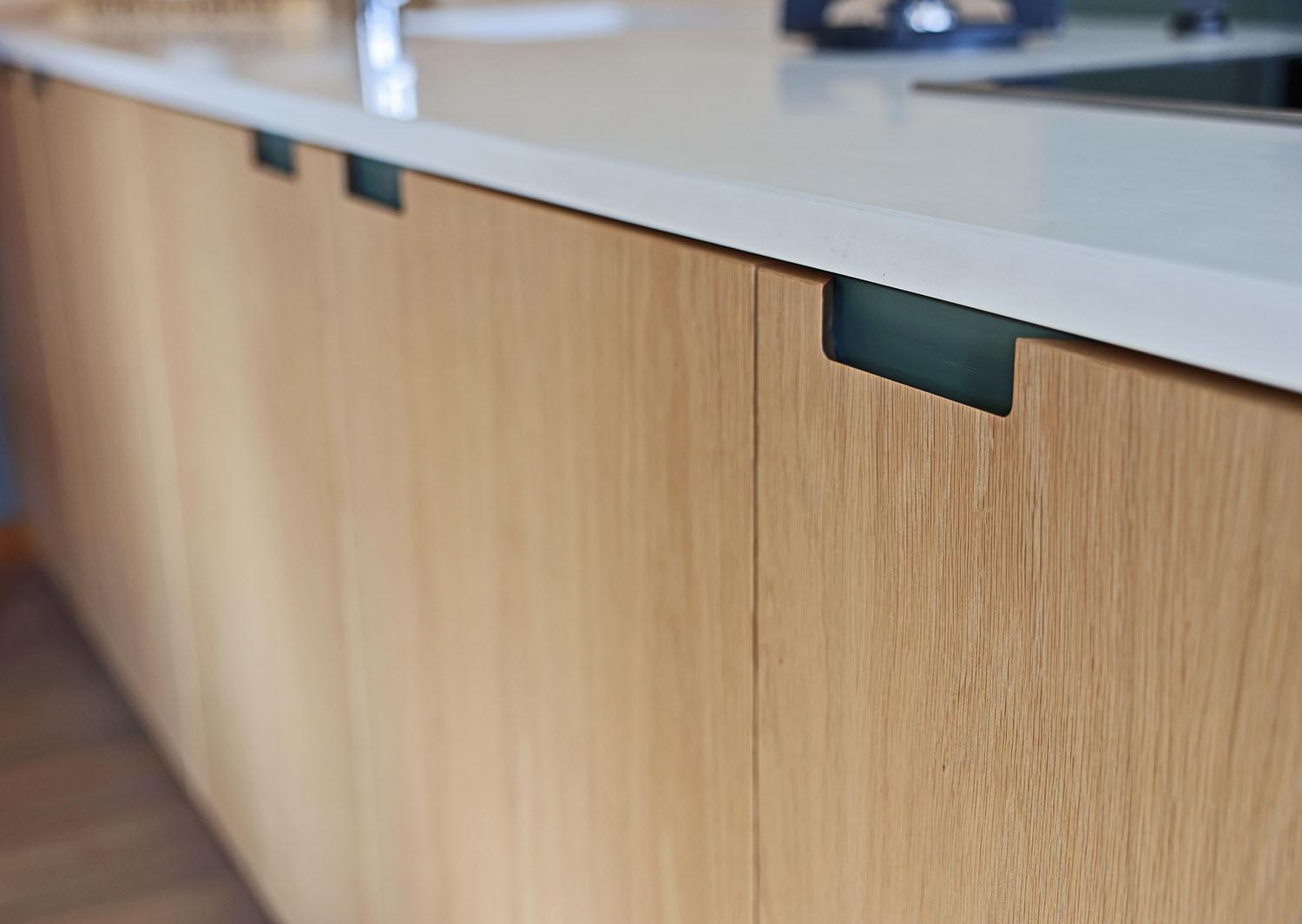Light wood kitchen cabinets with modern, minimalist design and integrated finger pull handles, topped with a smooth, white countertop.
