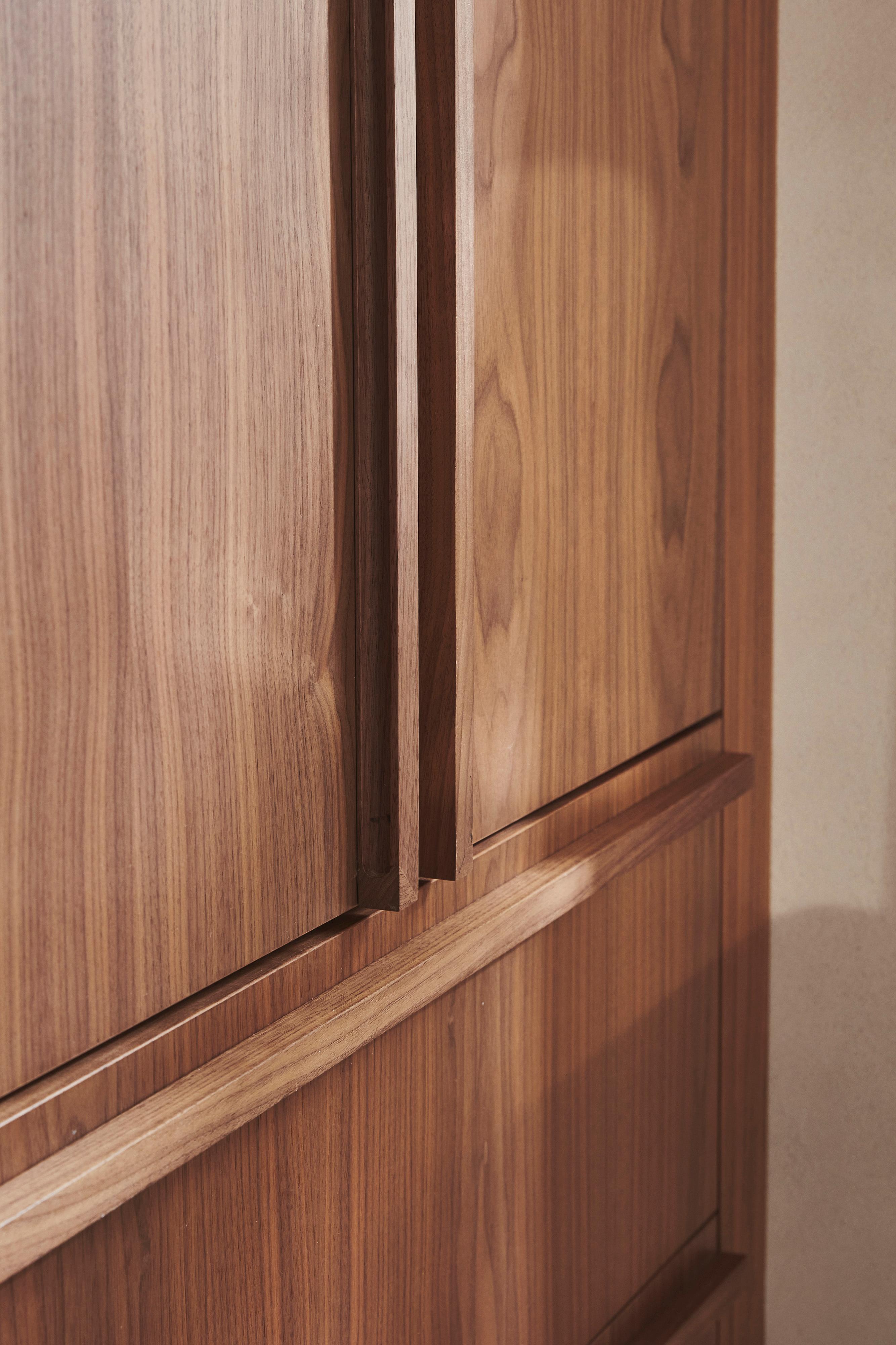 Close-up of a wooden cabinet with a smooth finish, showing a section of its doors and handles. The wood has a distinct grain pattern with warm, natural tones.
