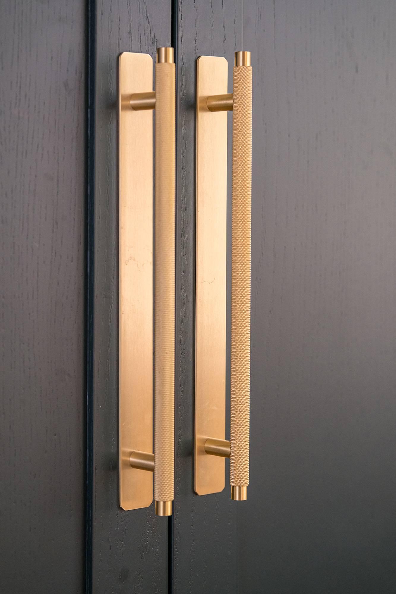Close-up of two vertical gold handles on a dark-colored cabinet or door, with a modern and sleek design.