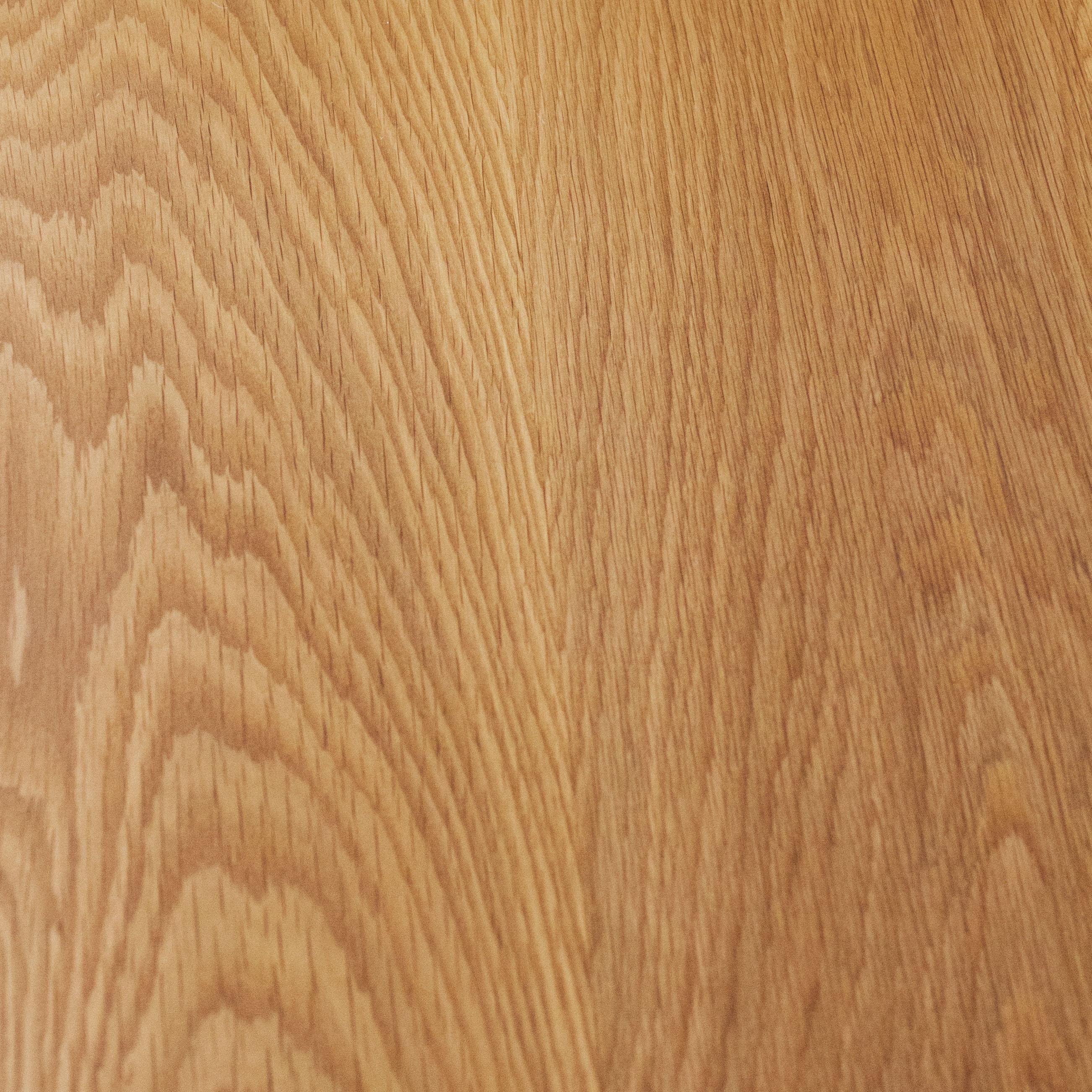 A close-up of a wooden surface showing the grain pattern. The wood features a light to medium brown hue with subtle variations and visible texture, highlighting the natural lines and striations typical of wood.