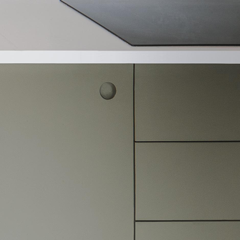 Minimalist photo showing part of a grey and white cabinet with flat surfaces, sharp lines, and a single round indented button detail near the top left corner.