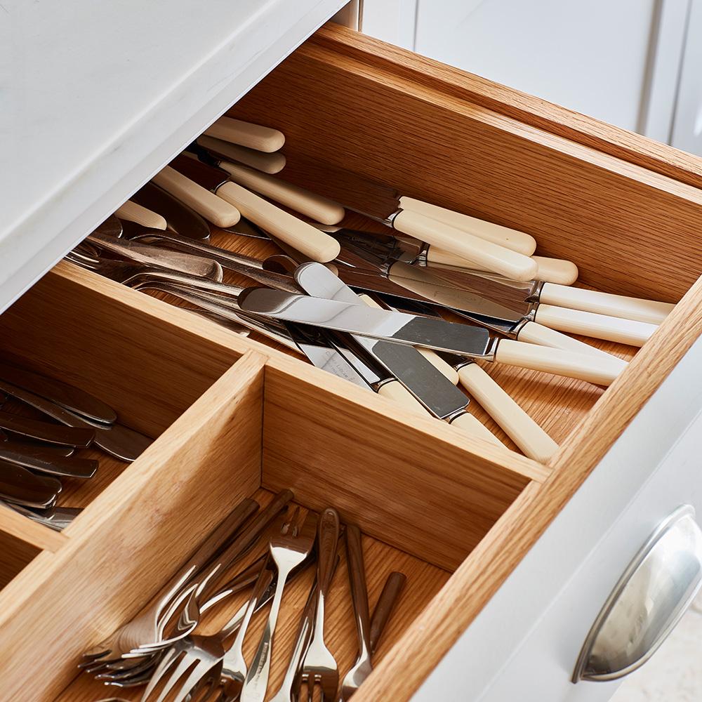 An open wooden kitchen drawer shows neatly organized forks and knives in separate compartments, with knives featuring both metal and cream-colored handles.