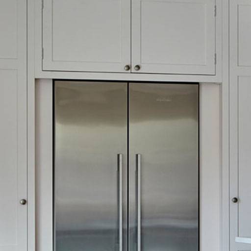 A modern stainless steel double-door refrigerator is built into white cabinetry with matching cabinet doors and silver handles above and beside it.