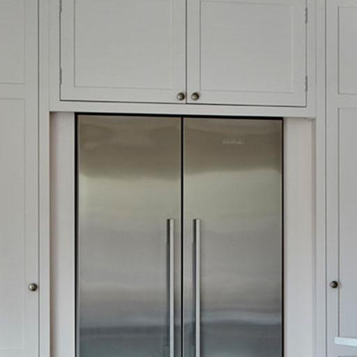 A modern stainless steel double-door refrigerator is built into white cabinetry with matching cabinet doors and silver handles above and beside it.