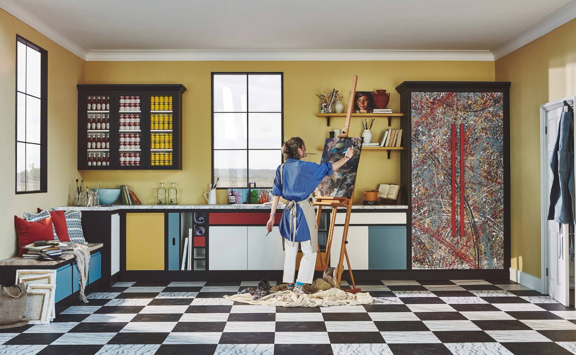 Modern kitchen studio inspired by Piet Mondrian, featuring primary colour-blocked cabinets and a checkered floor. An artist works at an easel, highlighting the kitchen as a creative workspace for bespoke design.