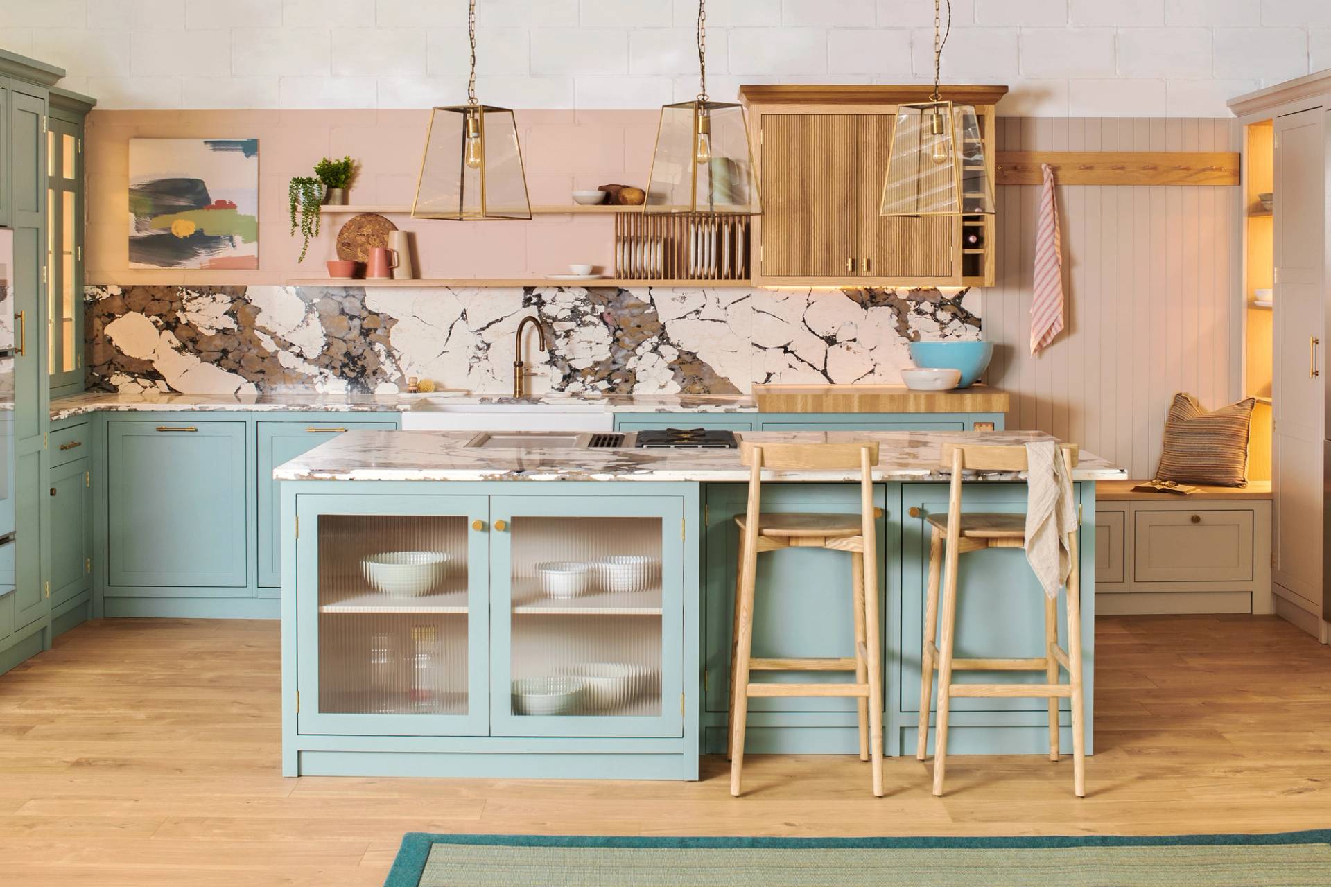 An eclectic contemporary kitchen features teal cabinetry, a bold marble backsplash, and a central island with fluted glass doors and wooden bar stools.