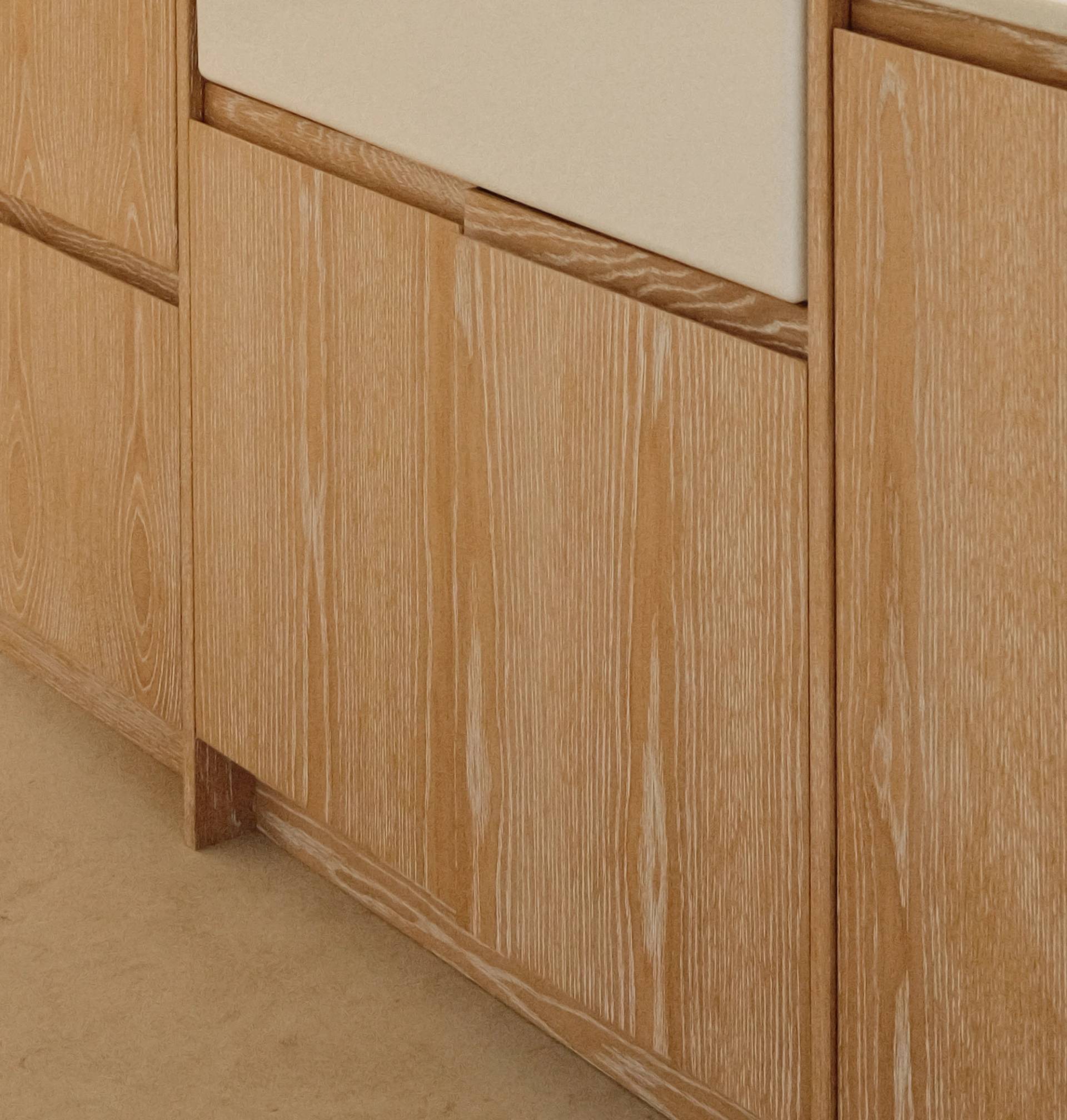Light wood cabinets with a visible natural grain pattern and vertical paneling, set against a beige floor. The cabinet doors have no visible handles, giving a minimalist appearance.